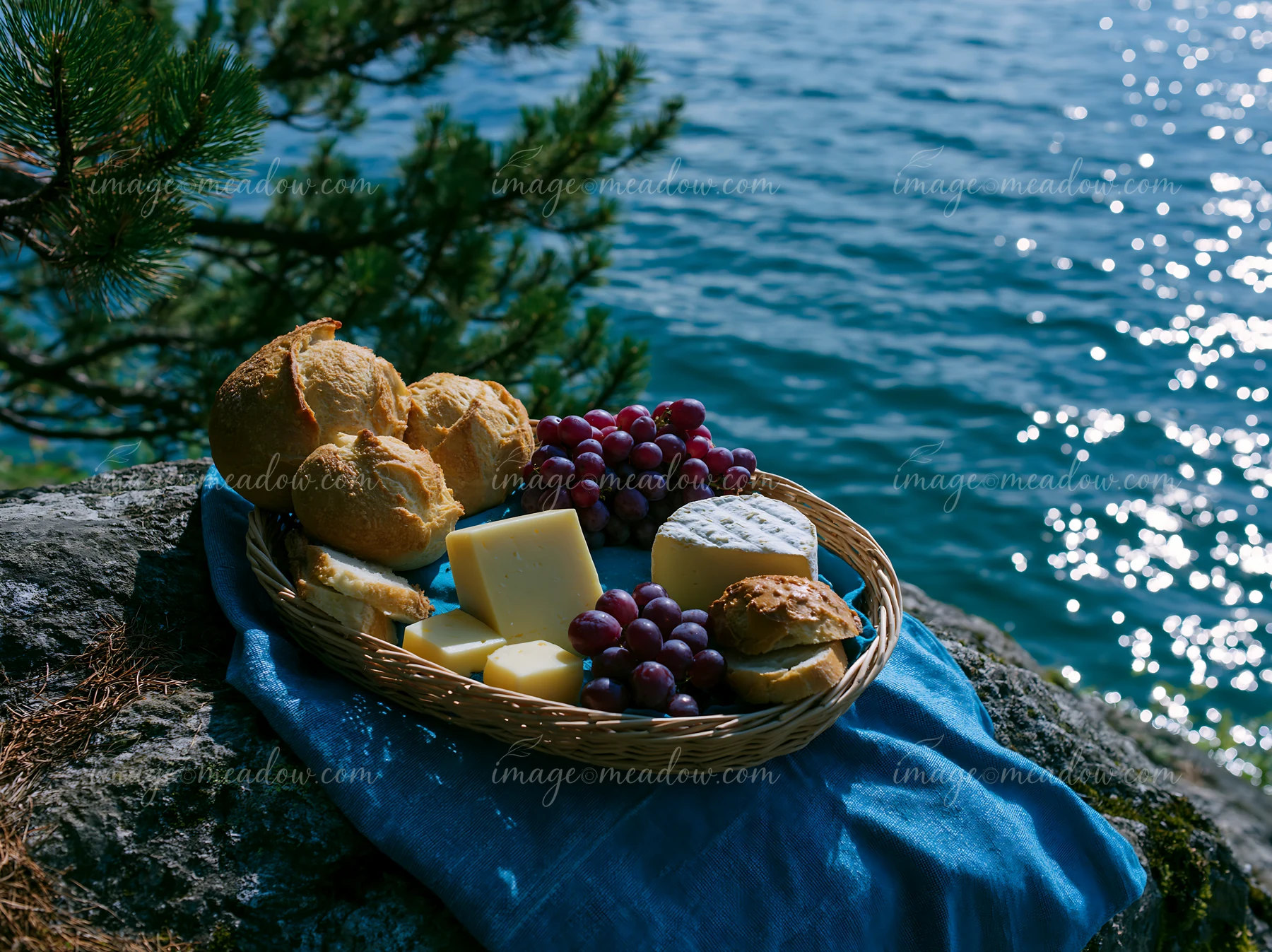 A picnic basket filled with cheese, bread, and grapes rests on a rock by an alpine lake.