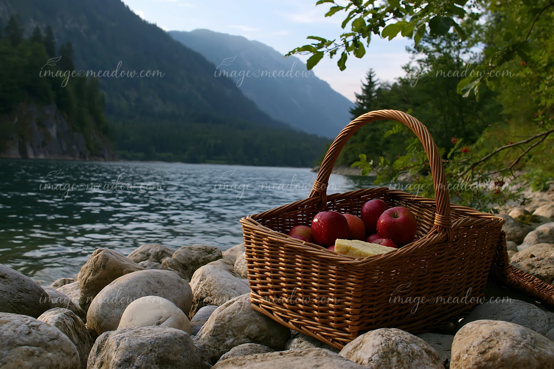 A picnic basket sits on rocks by an alpine lake, surrounded by mountains and trees.