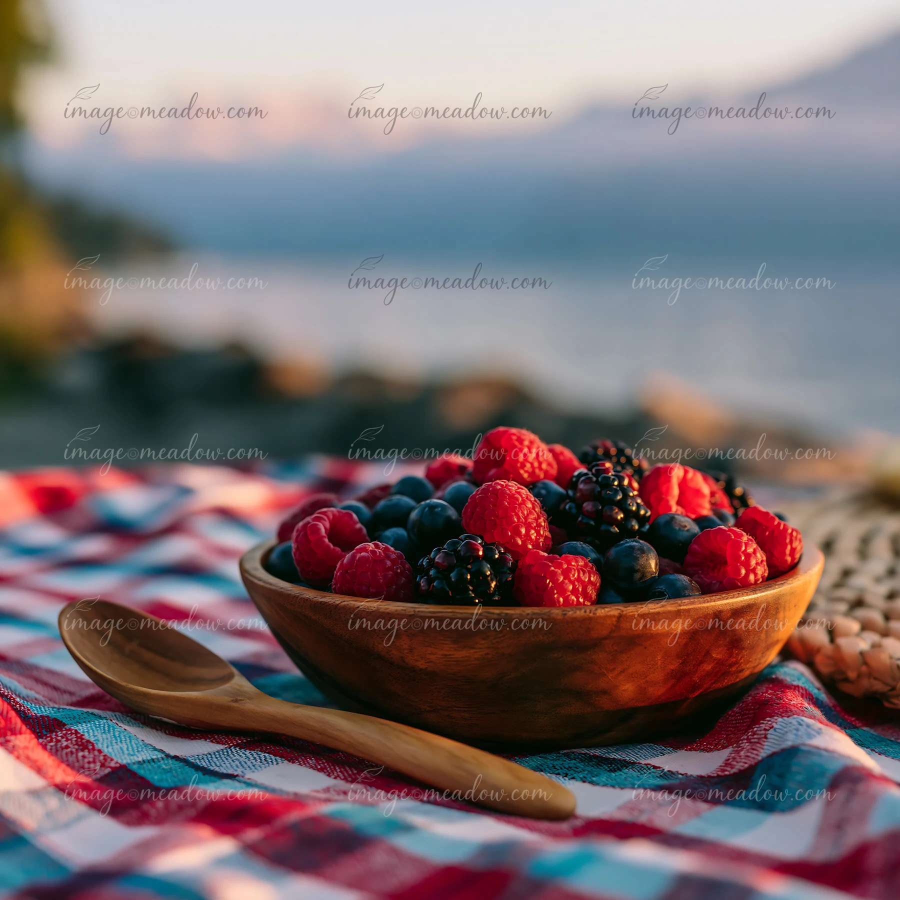 A picnic setting features a bowl filled with fresh raspberries, blueberries, and blackberries.