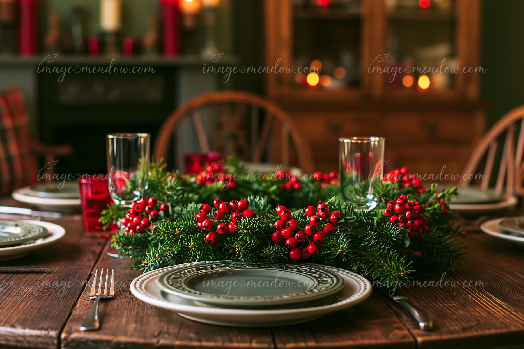 A pine wreath adorned with red berries is placed on a wooden table set for a meal.