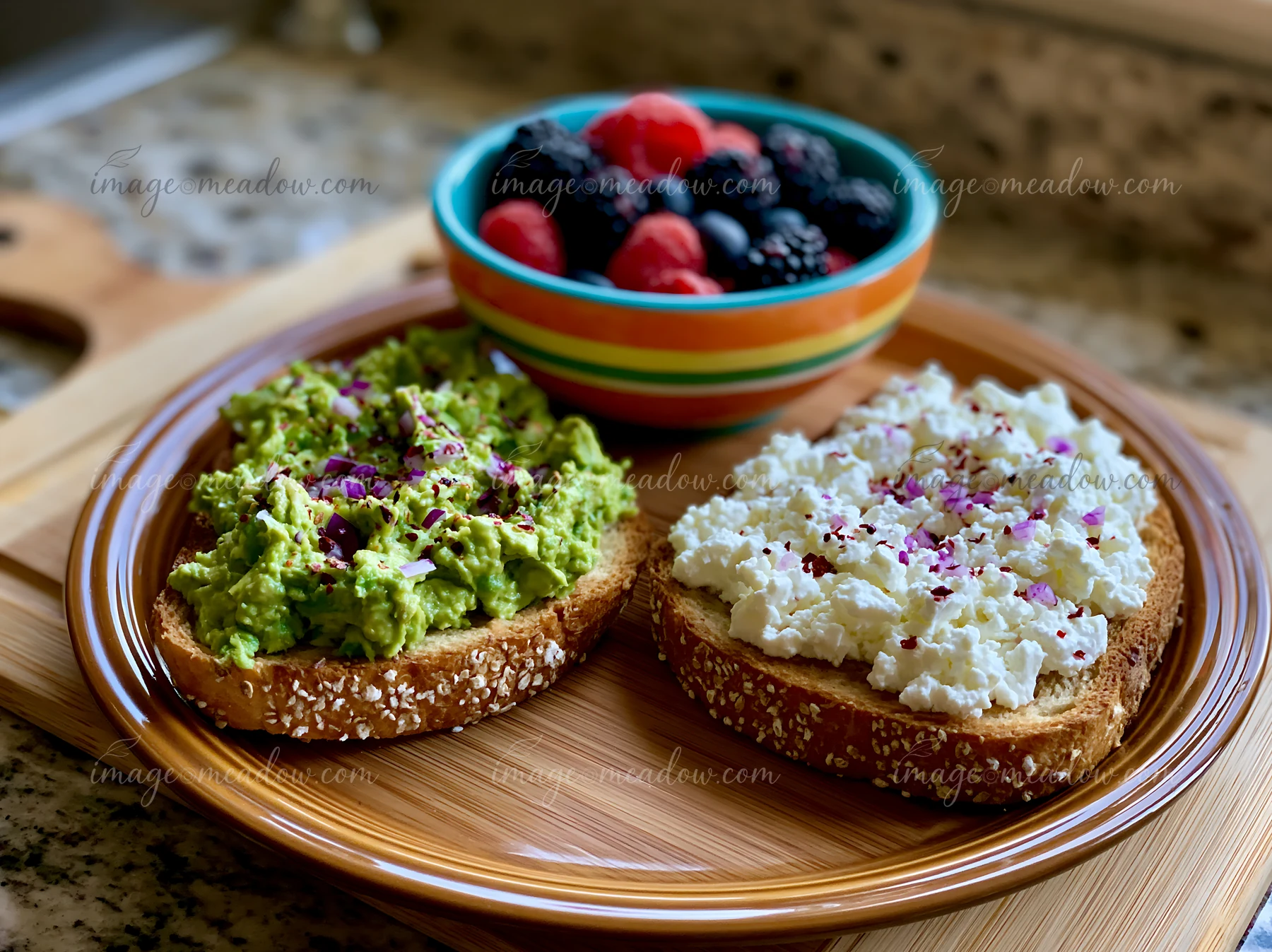 A plate holds two slices of whole grain bread topped with mashed avocado and seasoned cottage cheese, alongside a bowl of mixed fresh berries.