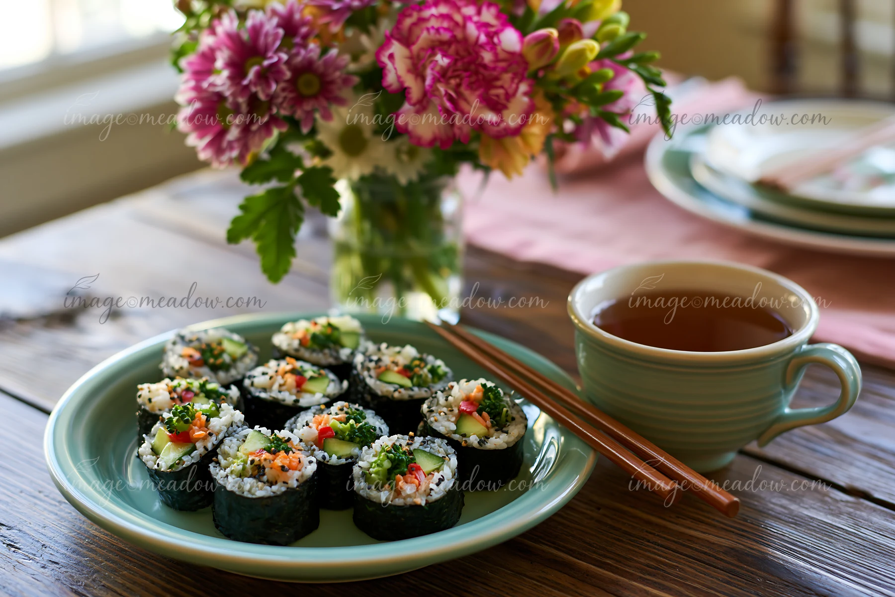 A plate of sushi served with tea is placed on a wooden table.