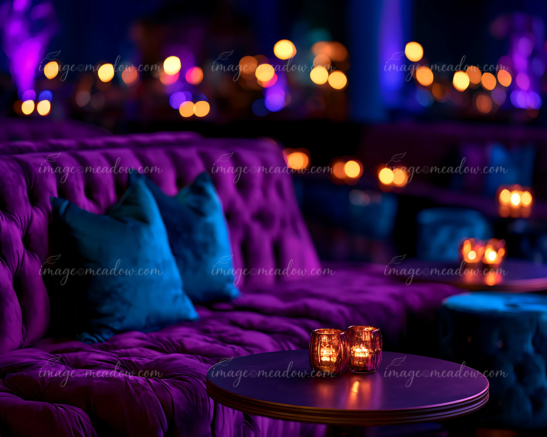 A plush couch and small tables are set in a lounge area with soft purple and blue lighting.