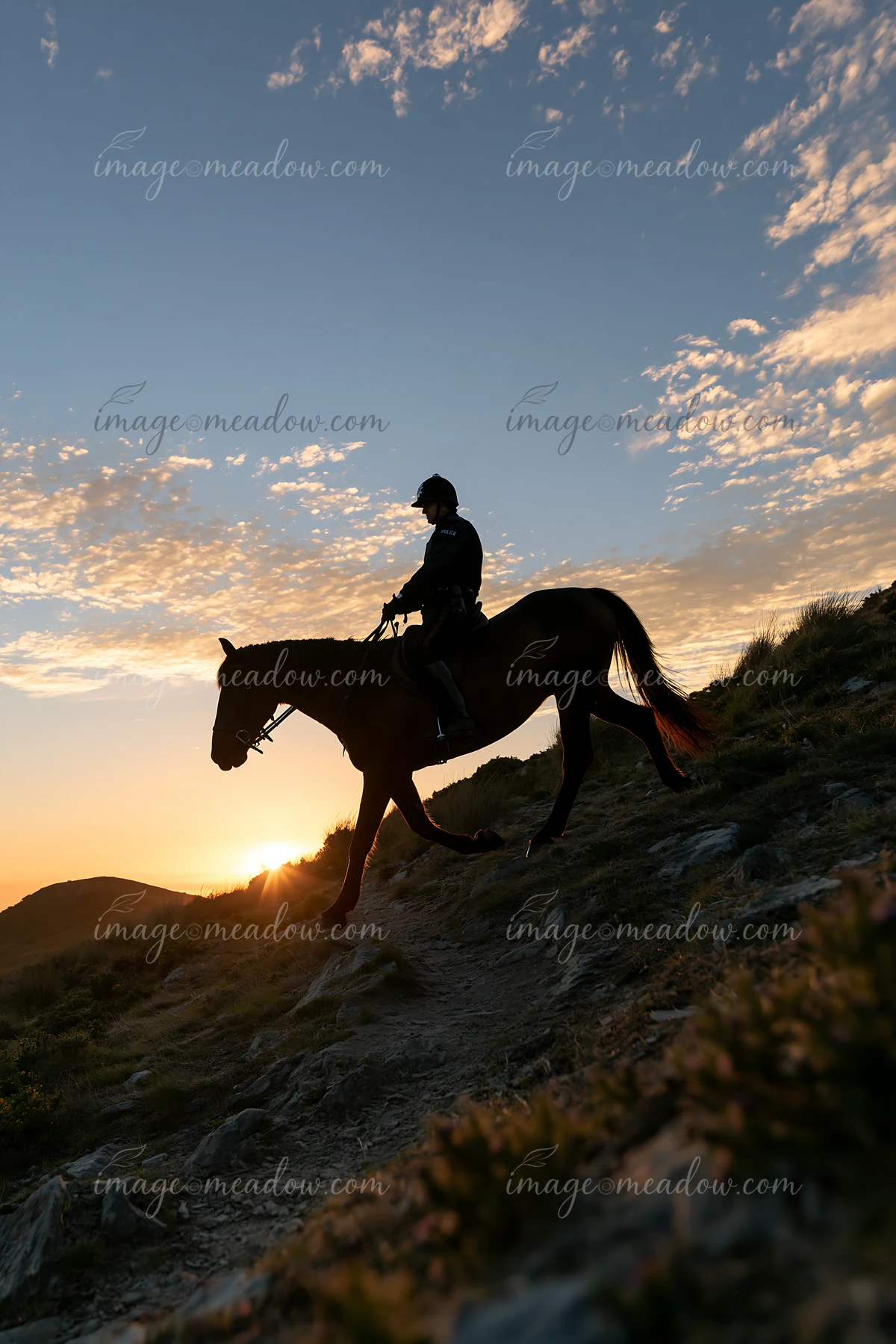 A police horse and rider travel along a rocky path as the sun sets in the background.