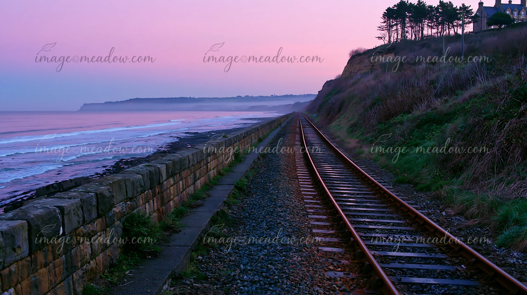 A railway track runs alongside a coastline with protective sea wall.