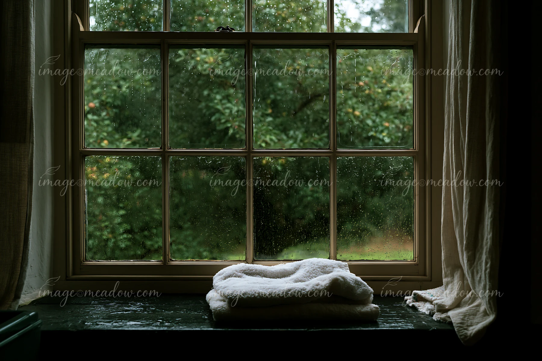 A rain-soaked wooden window in a rural home shows blurred greenery outside.