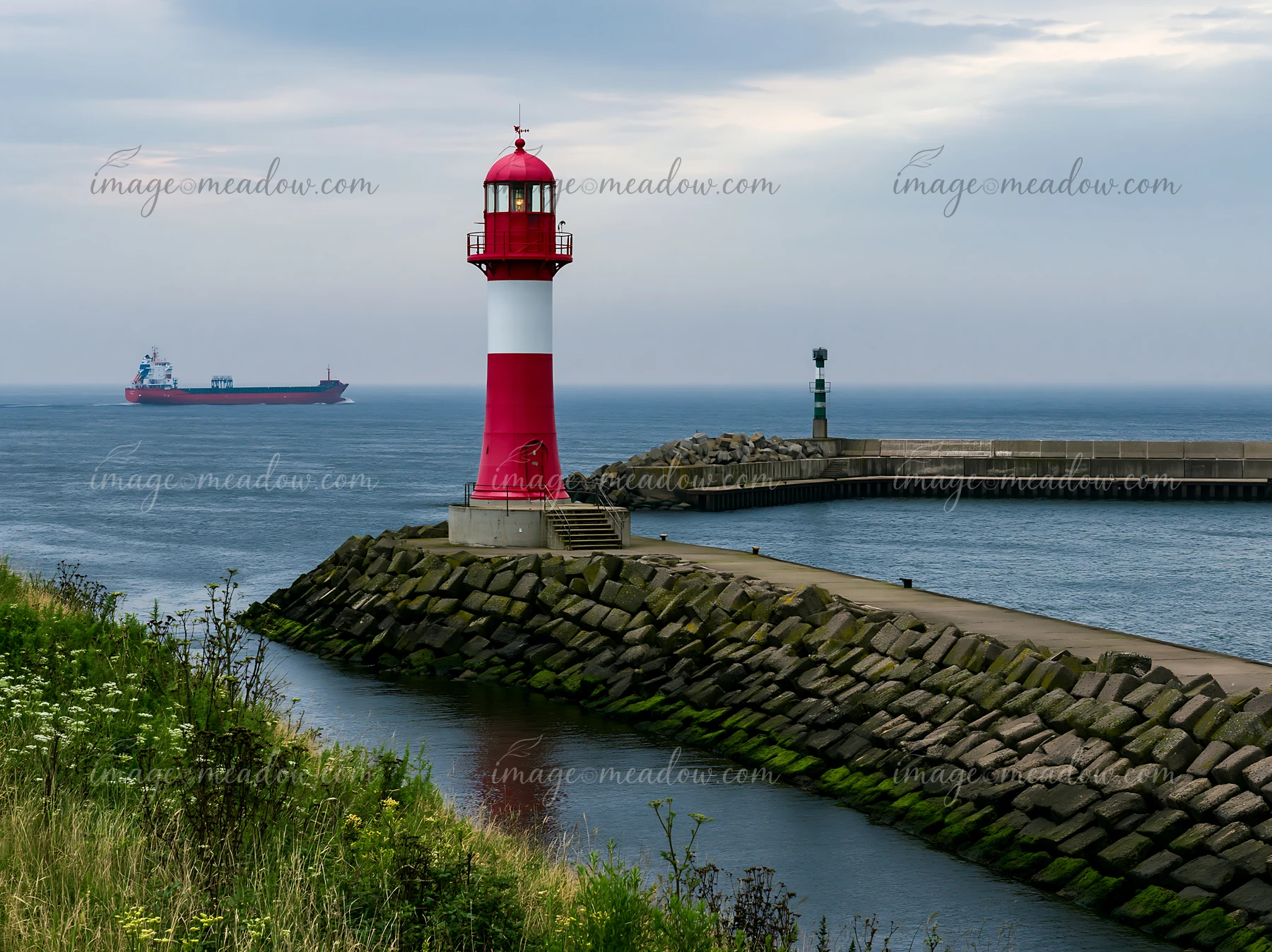 A red and white lighthouse stands on a rocky coastline covered in sea fog, guiding ships in an overcast setting.