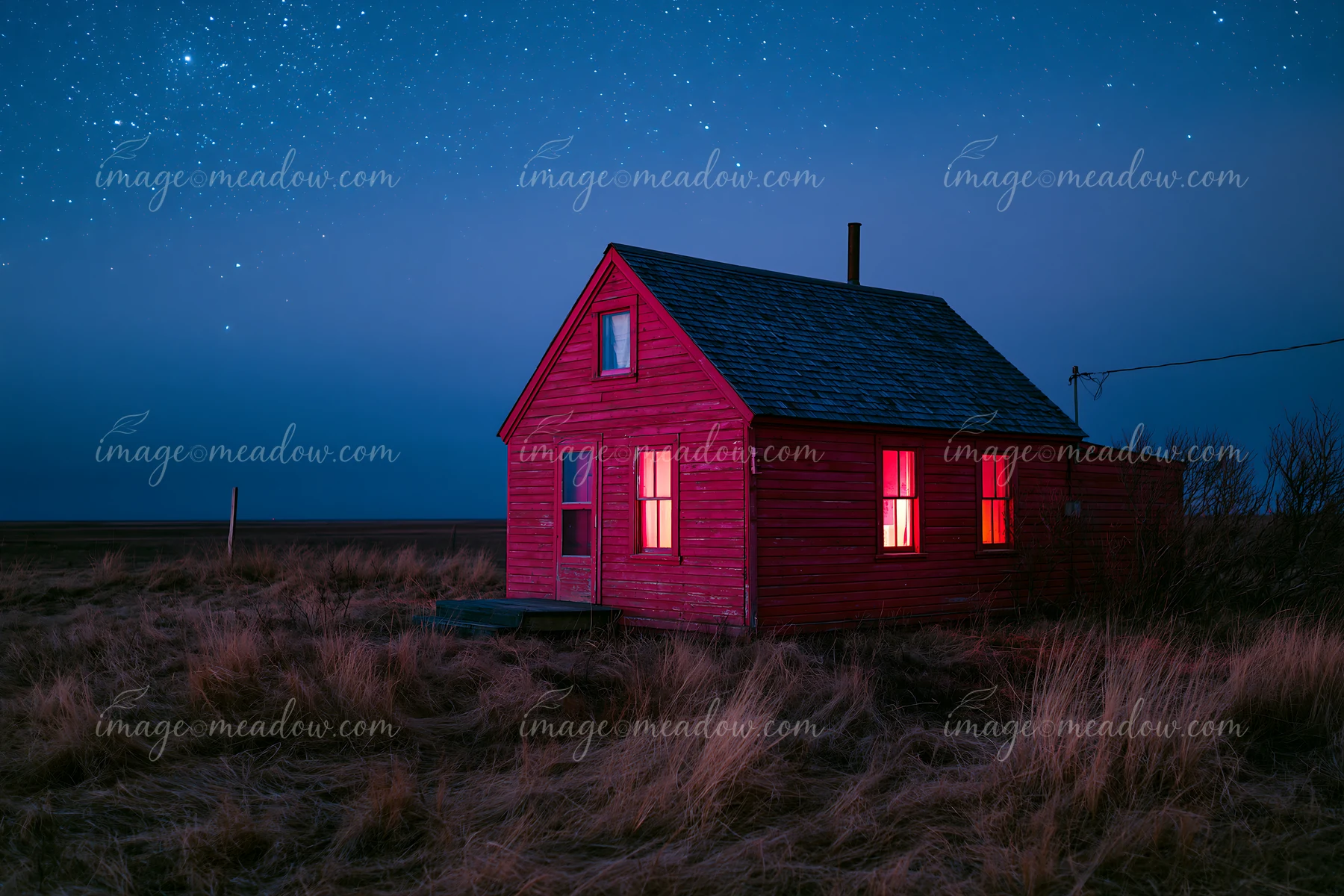 A red cabin stands alone in a grassy field as stars fill the night sky.