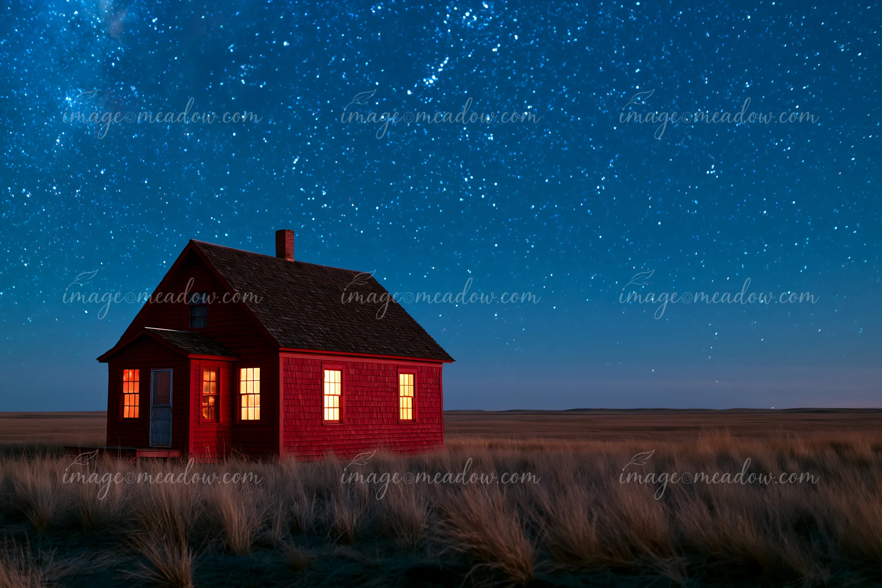 A red cabin stands alone in an open field with glowing windows.