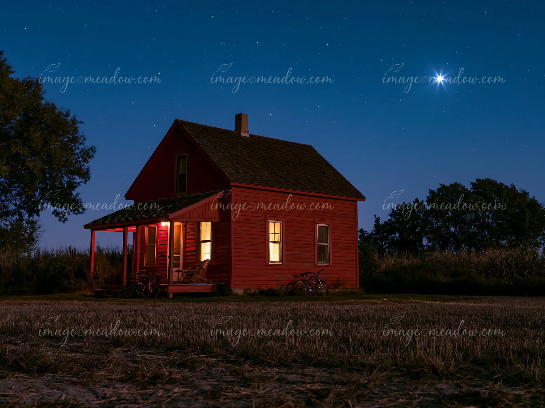 A red house stands alone under a starry sky in a rural setting.