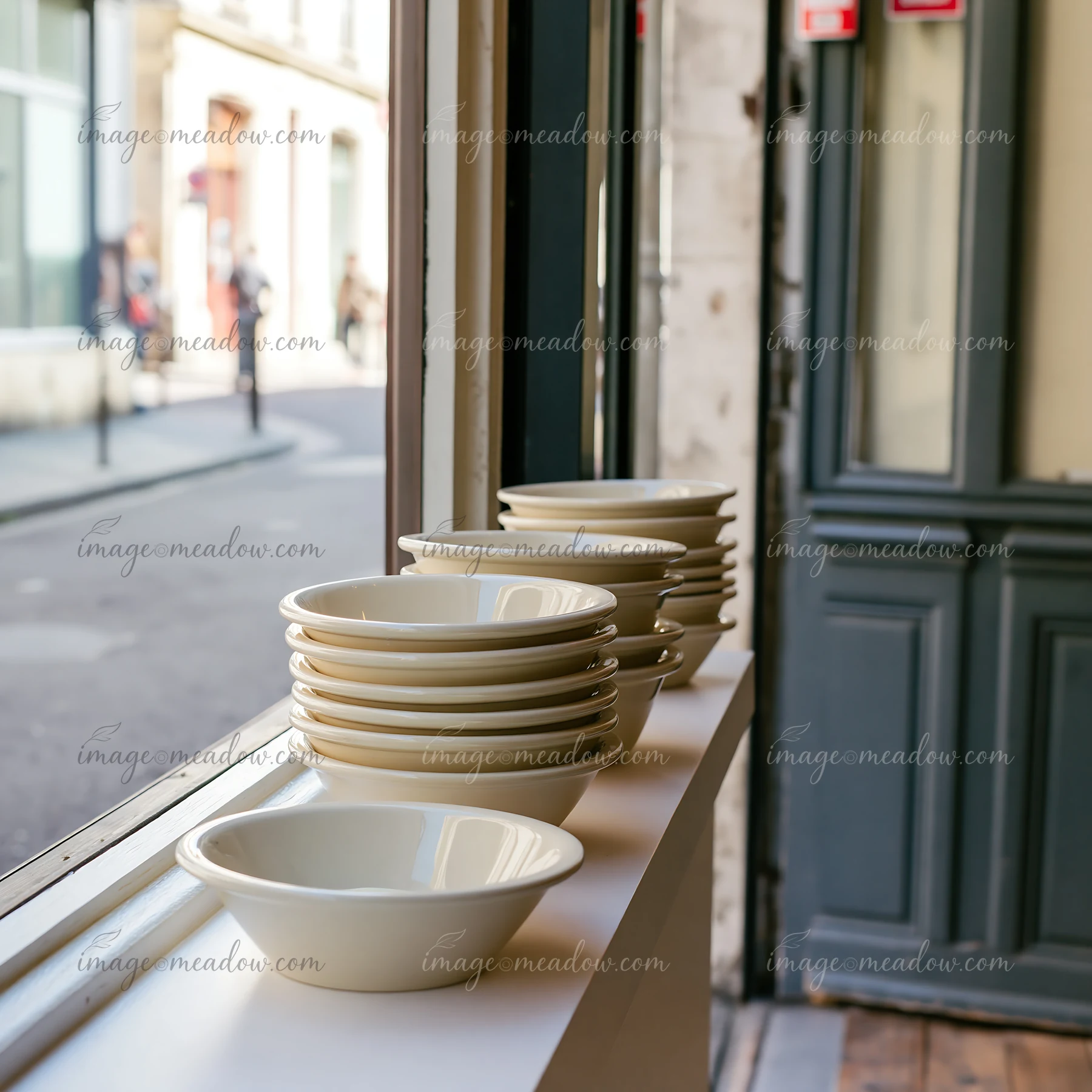 A row of ceramic bowls sits on a window ledge in a dairy products shop on a pedestrian street.