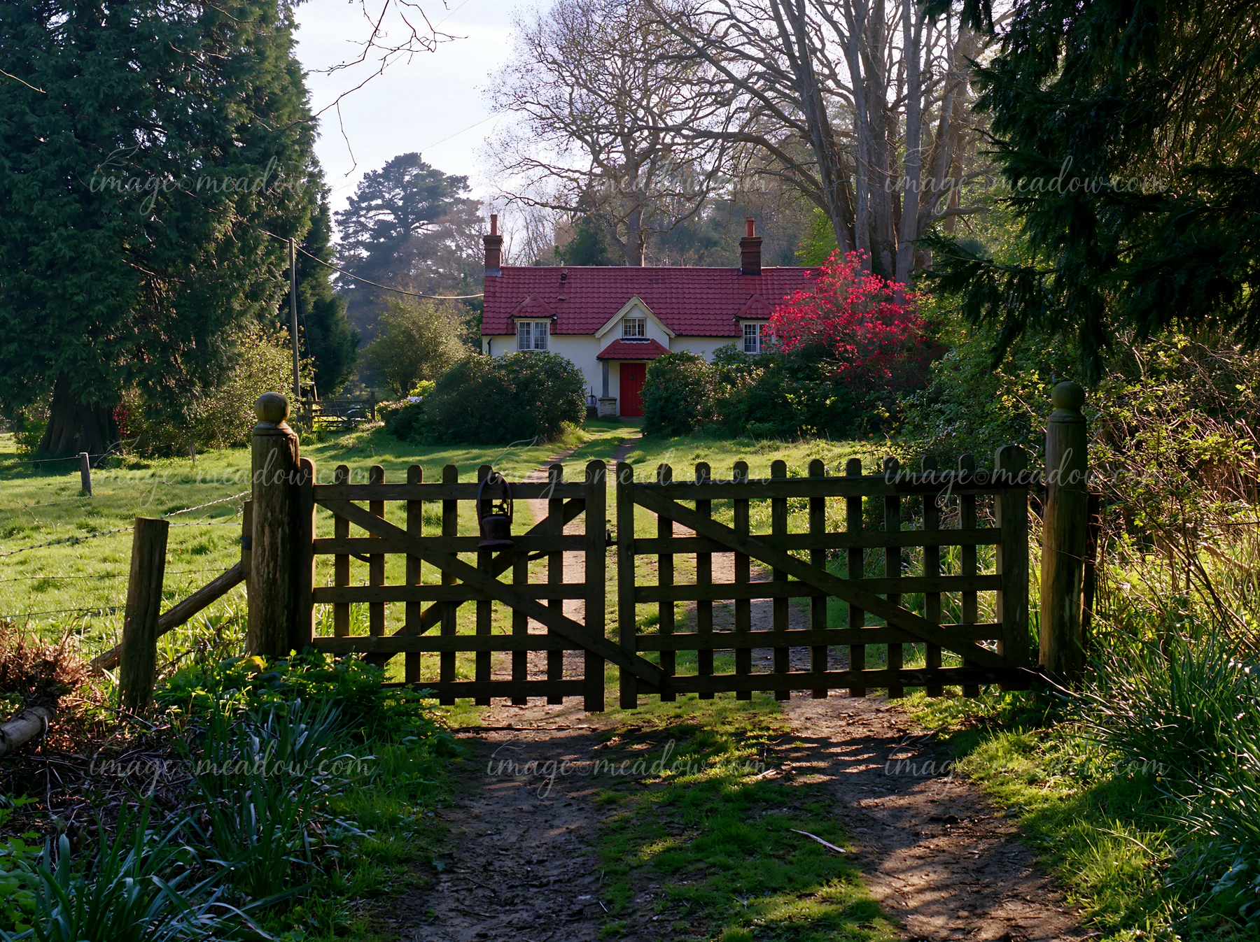 A rural cottage is seen through a wooden gate along a dirt path.