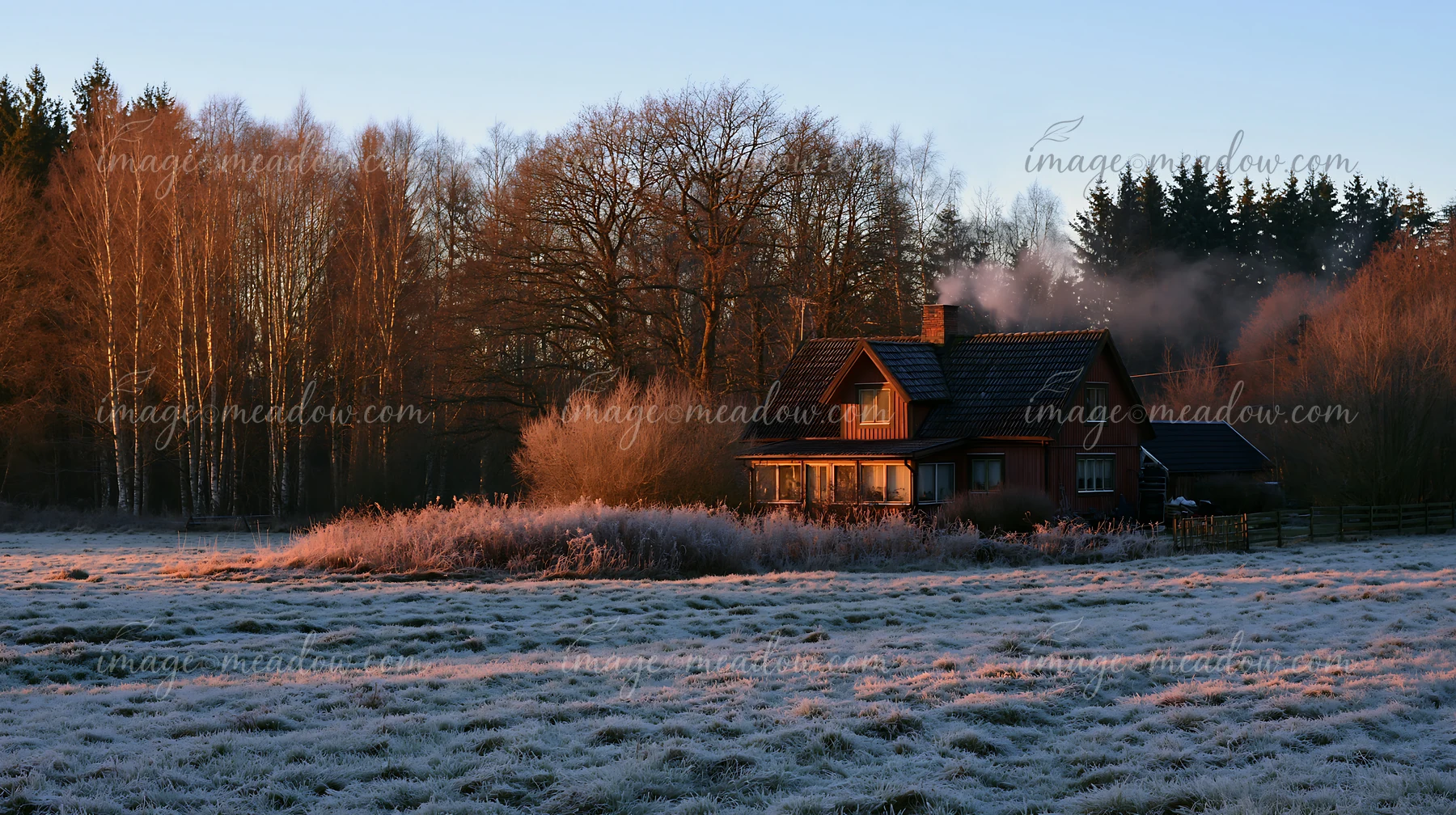 A rural cottage with chimney smoke stands among frost-covered grass and trees at dawn.