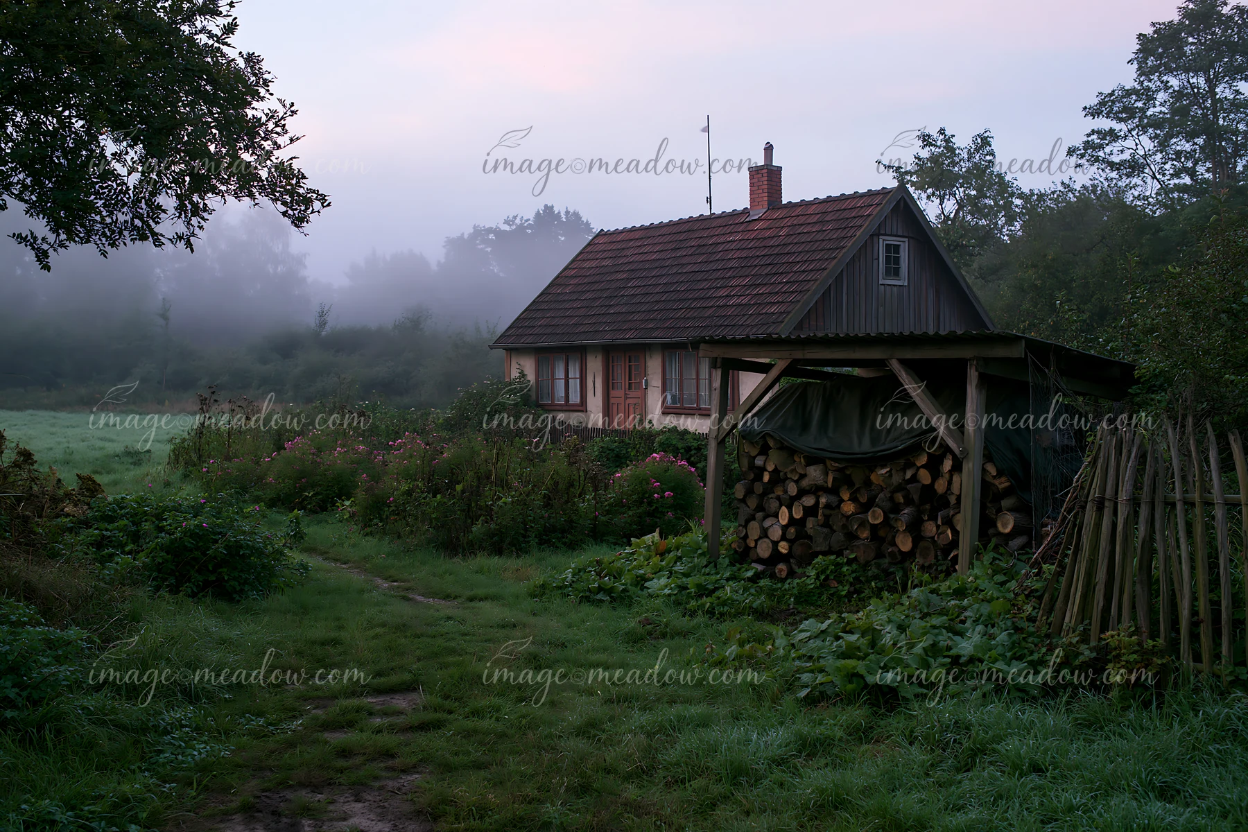 A rural cottage with firewood stack sits surrounded by greenery.