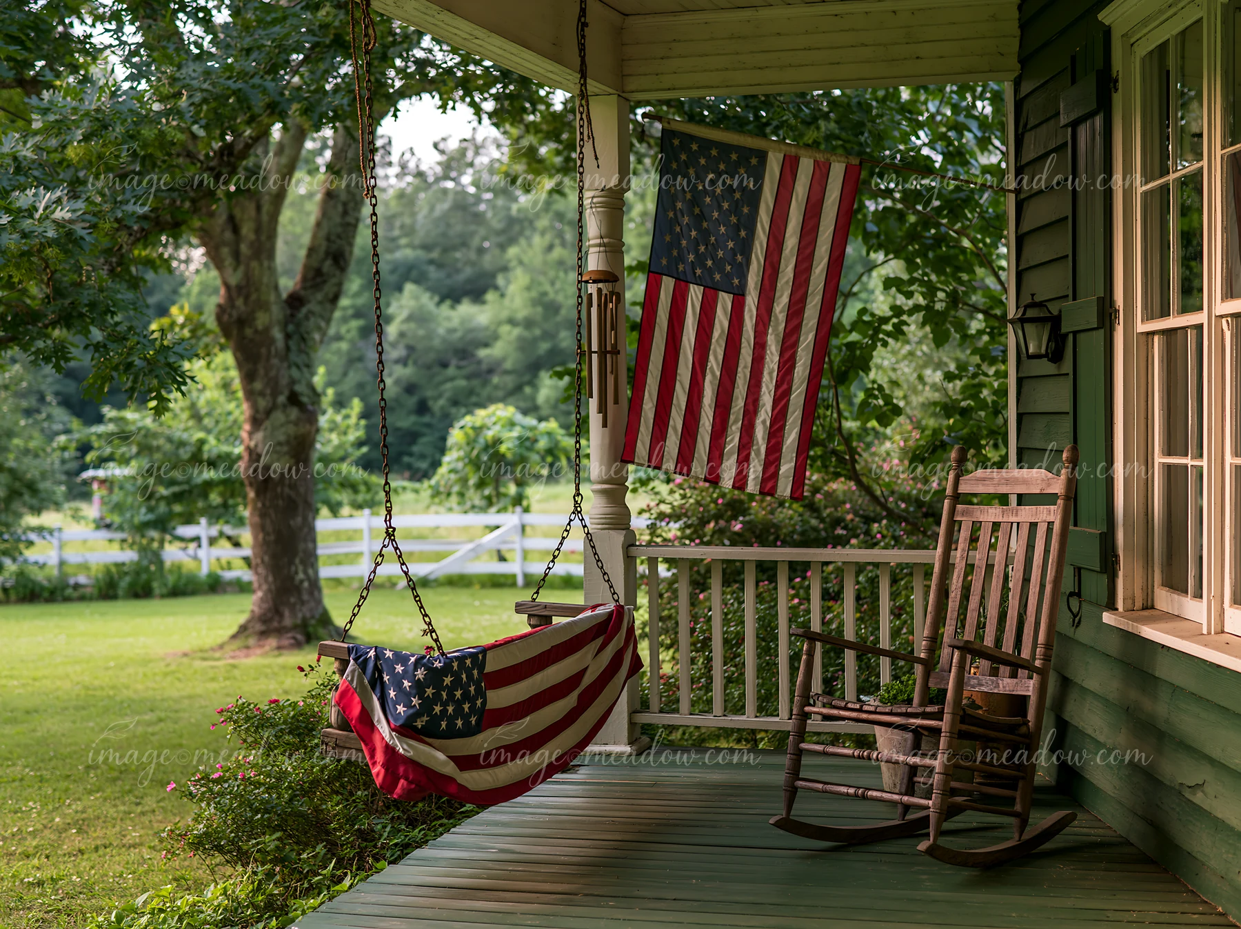 A rural farmhouse features a prominent American flag hanging from the porch, alongside a swing and rocking chair.