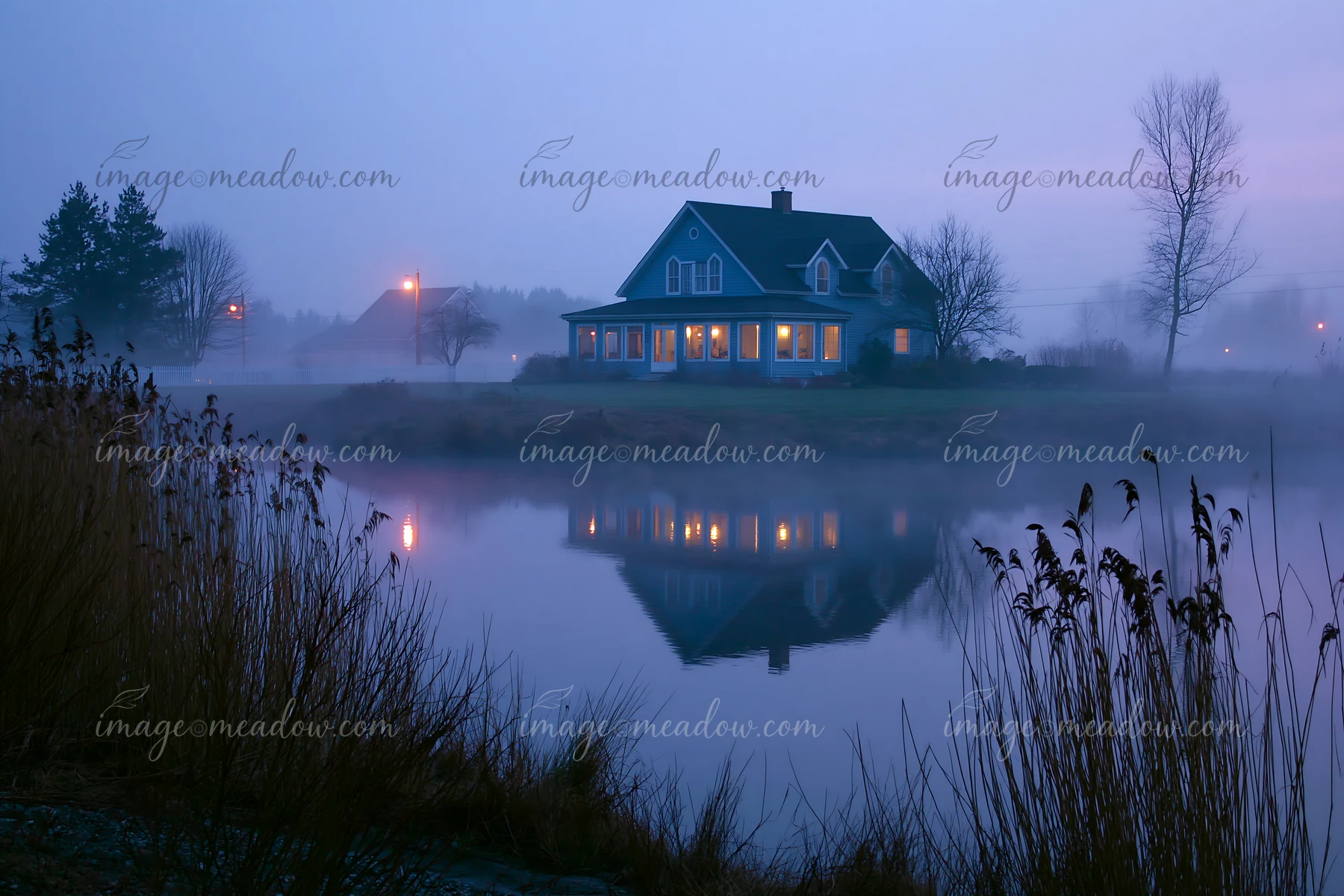 A rural farmhouse in morning fog stands by a quiet lake.