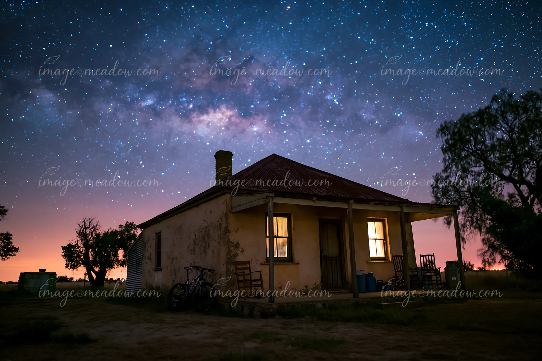 A rustic farmhouse stands under a bright night sky filled with stars and the Milky Way.
