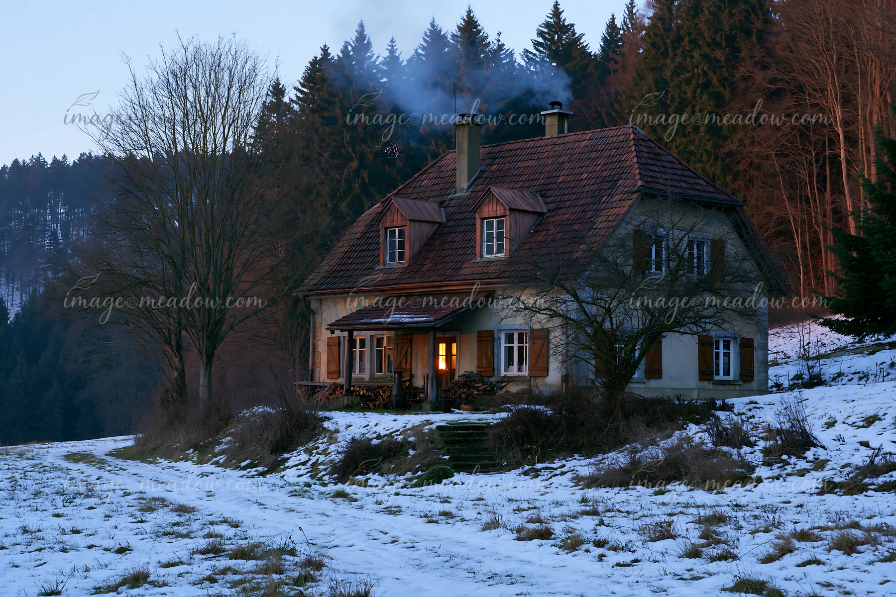 A rustic house with wooden shutters stands in a snowy landscape near a forest.