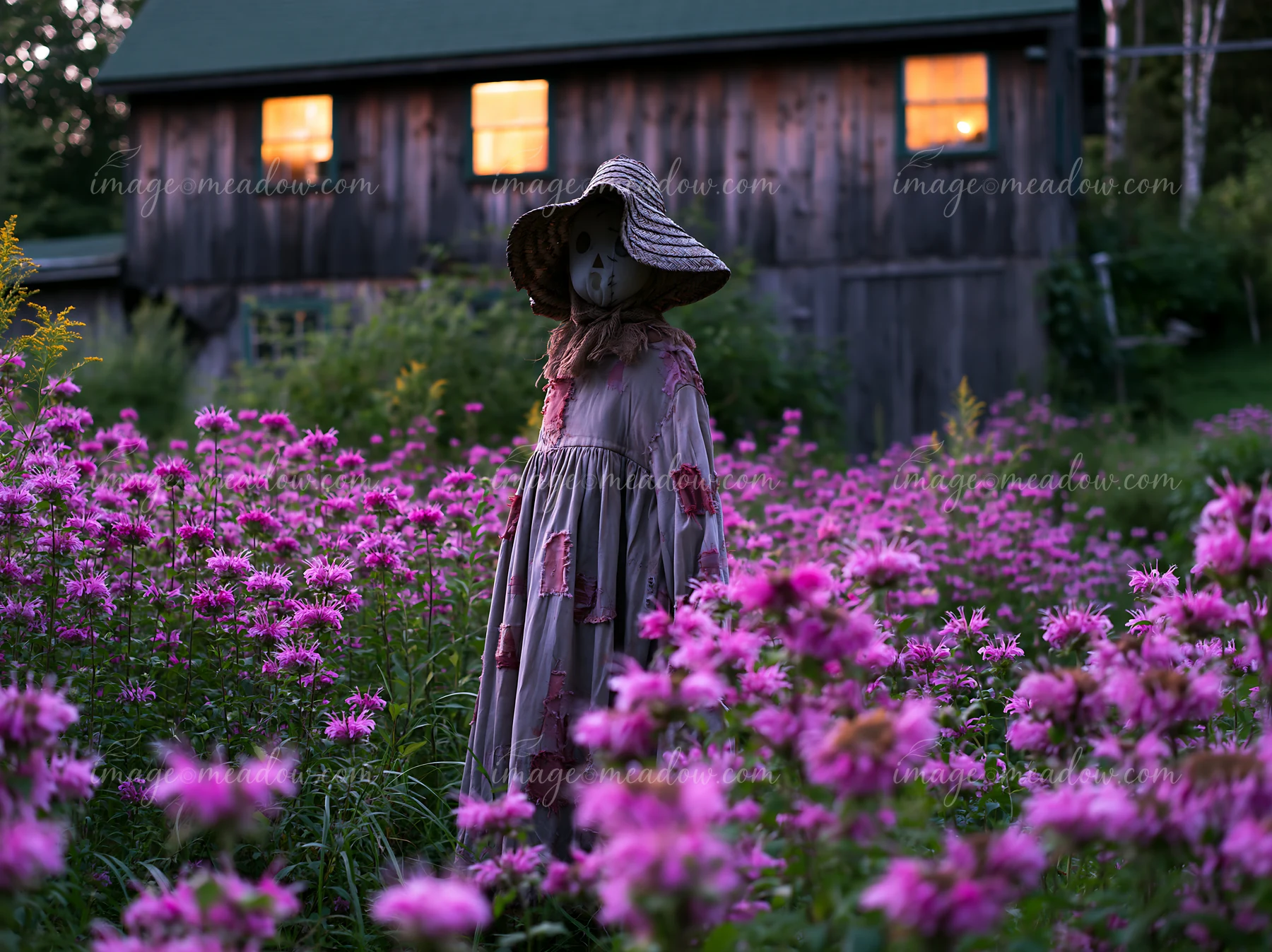 A scarecrow stands among blooming wildflowers in a field next to a rustic cabin.