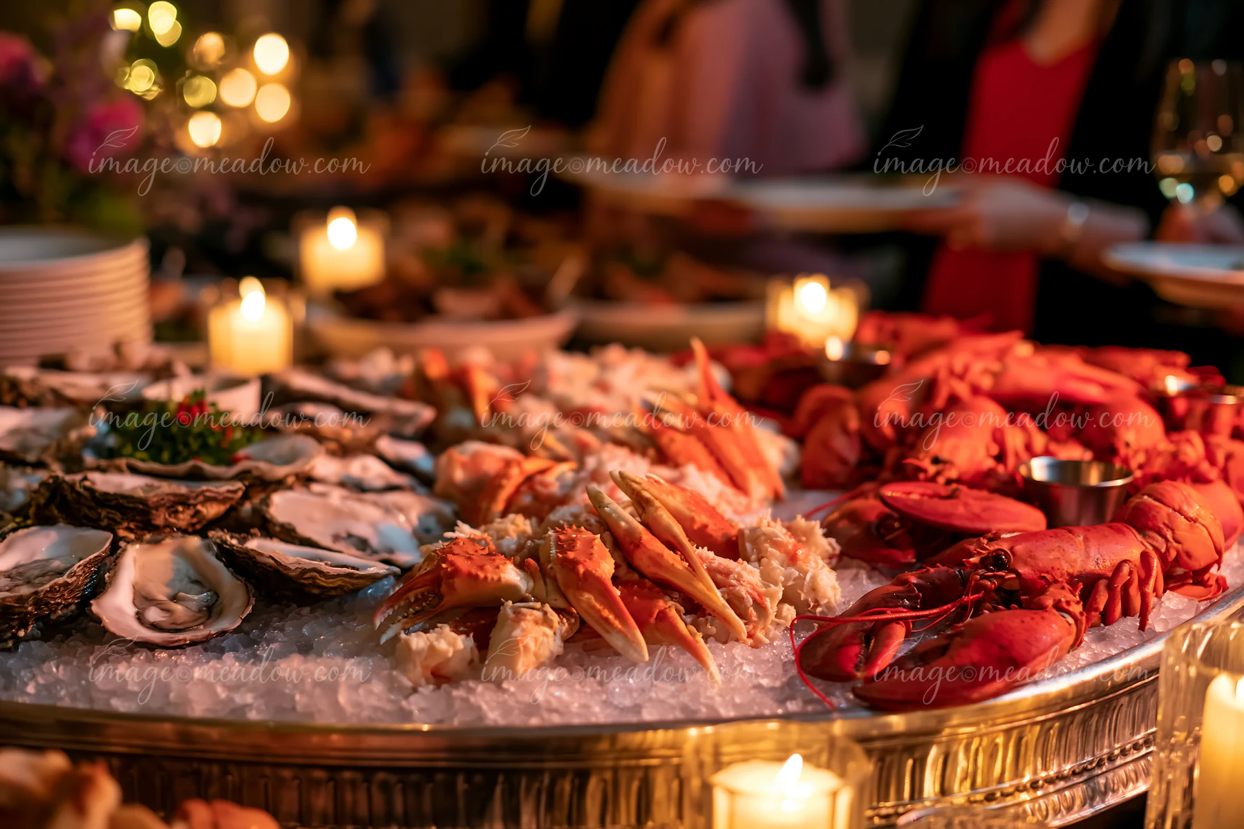 A seafood buffet features a variety of chilled seafood on ice, including crab, lobster, and oysters, arranged next to lit candles in an elegant setting.
