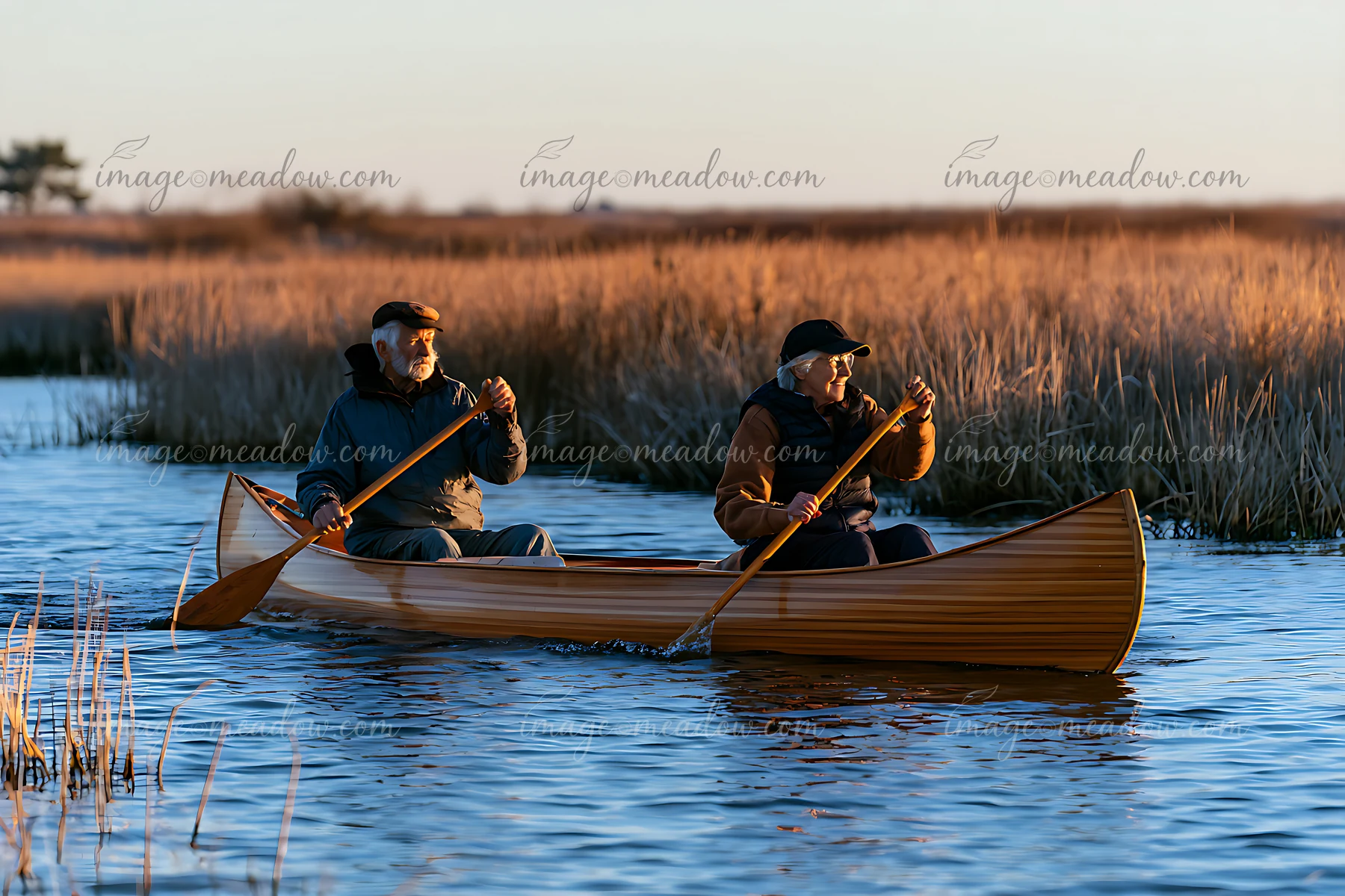 A senior couple is paddling a canoe through wetlands with tall grass.