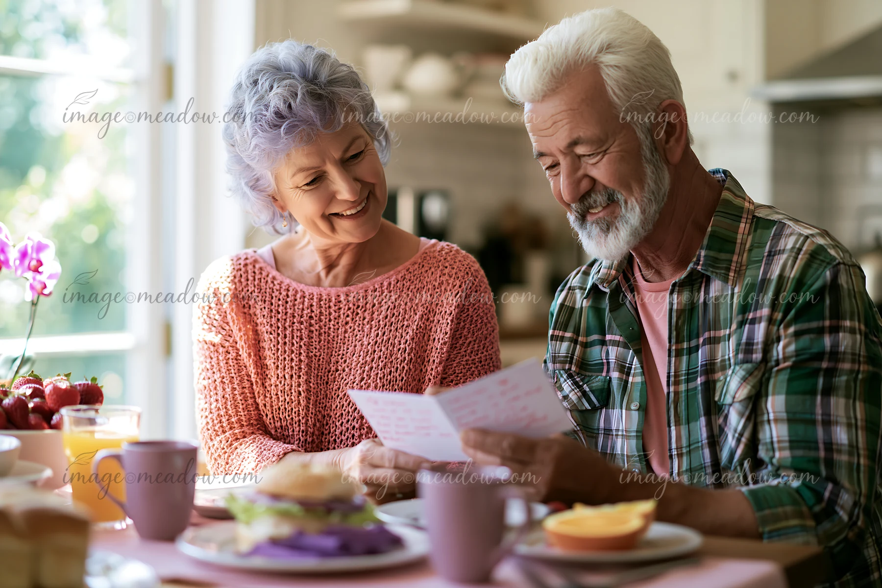 A senior couple sits at a dining table in their kitchen, sharing a meal while reading an anniversary card together.