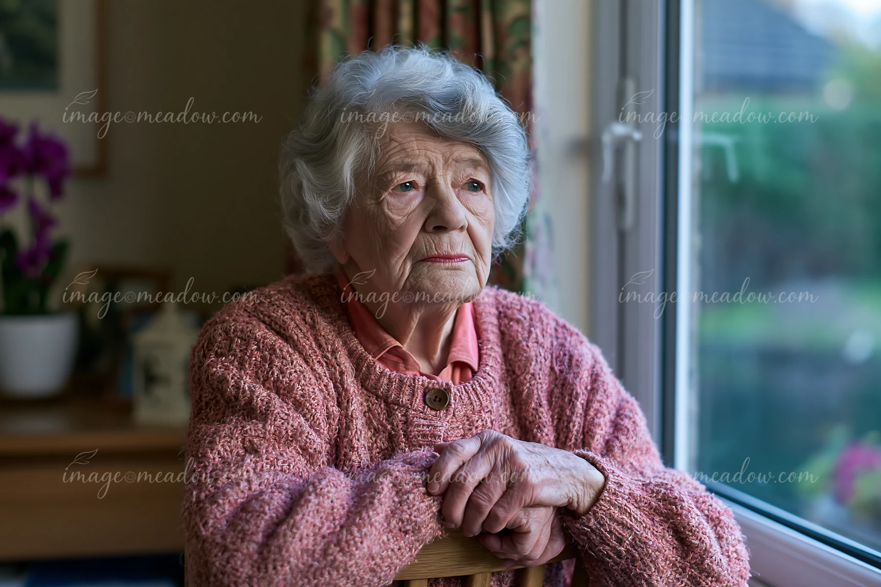 A senior with Alzheimer's looking out a window in a well-lit room.