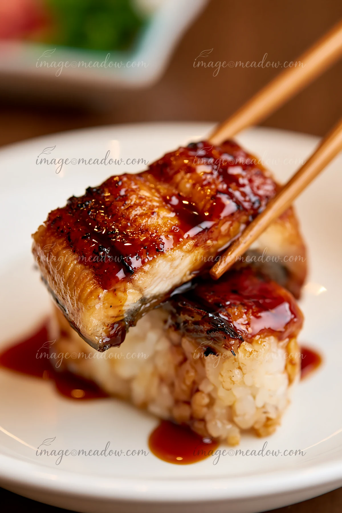 A single piece of eel nigiri with sauce is held by chopsticks.