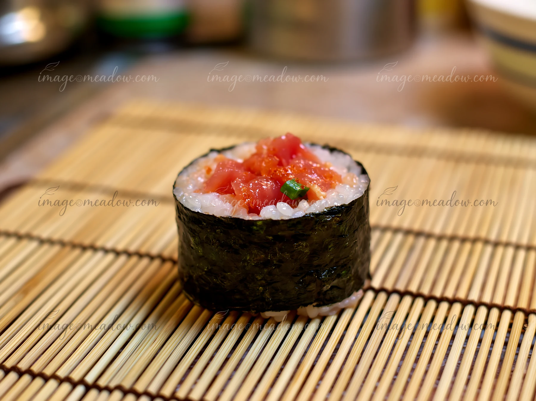 A single spicy tuna roll piece sits on a bamboo mat, showcasing the rice and tuna filling.