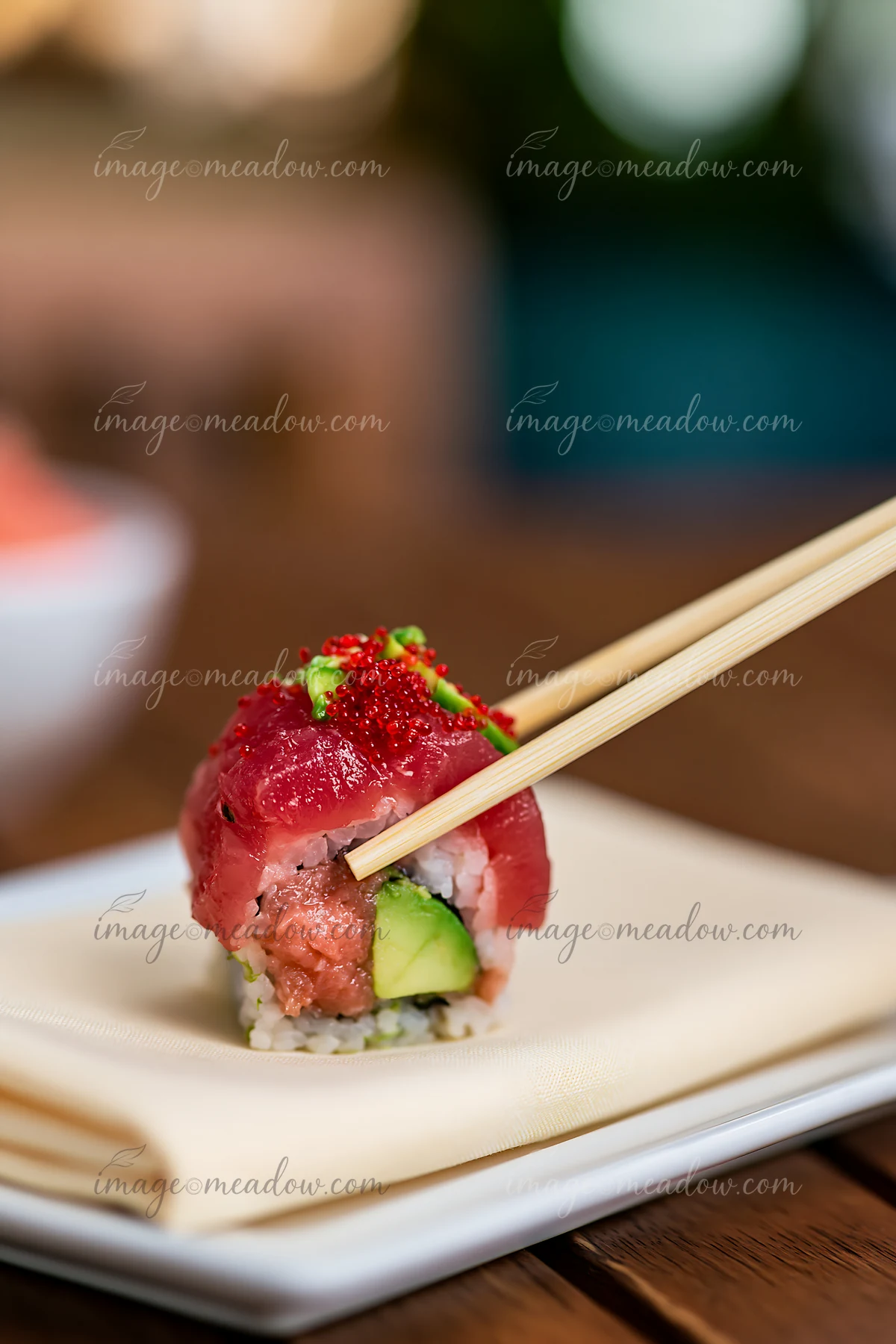 A single sushi piece with chopsticks held above a white plate.