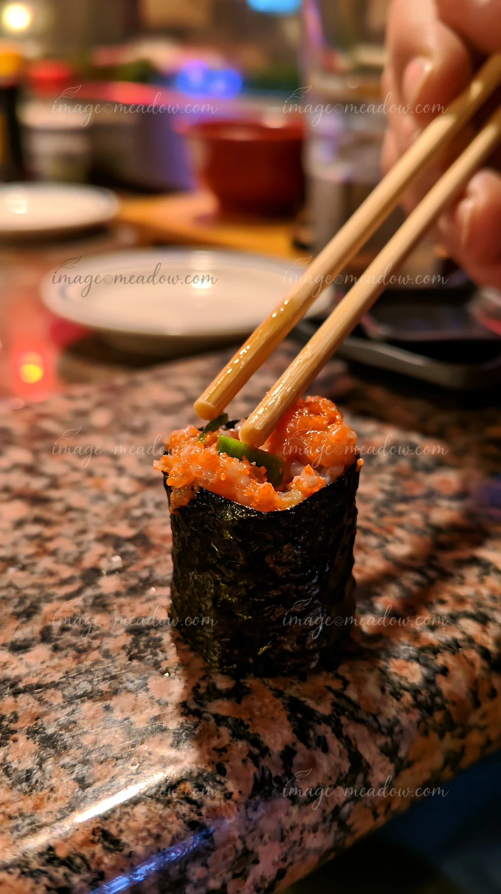 A single sushi piece with chopsticks is being picked up on a textured granite surface.