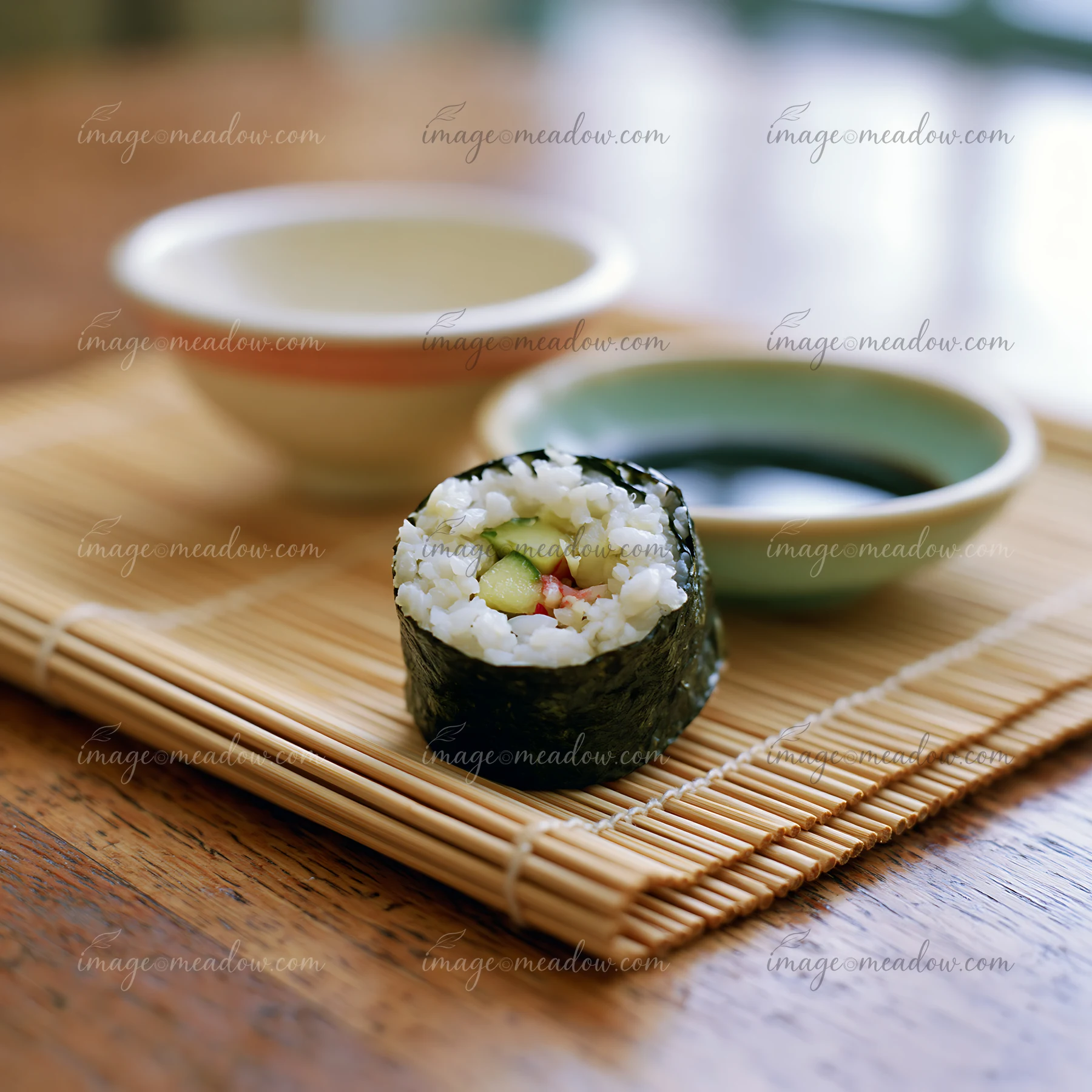 A single sushi roll on a bamboo mat is ready to eat alongside small bowls of soy sauce.