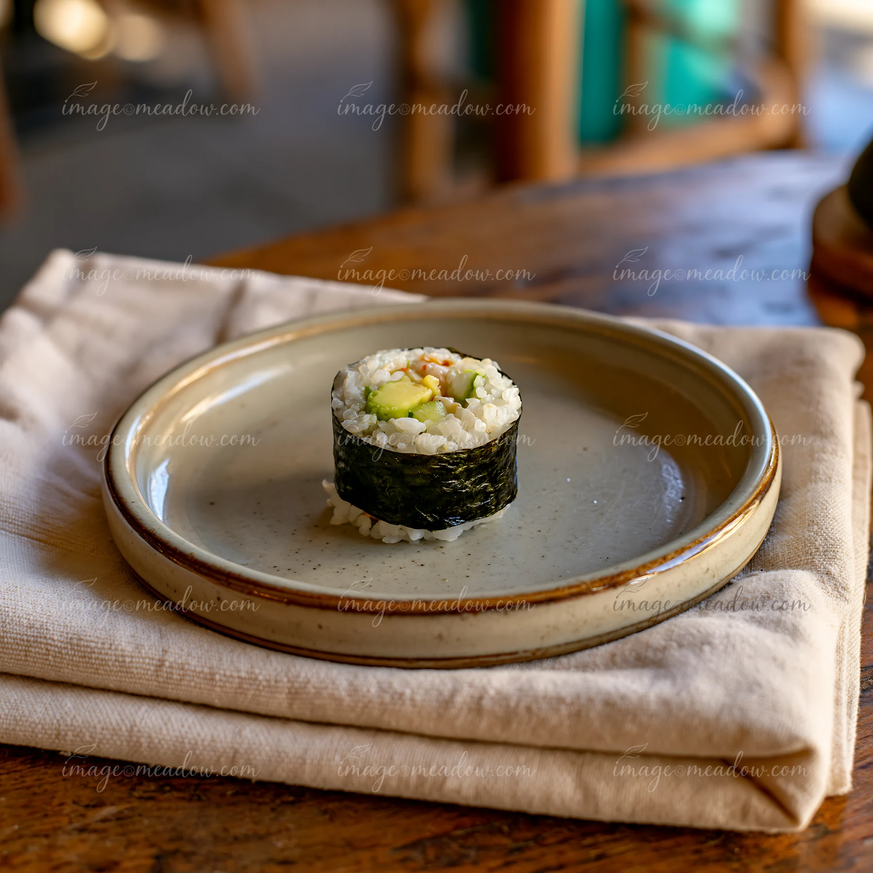 A single sushi roll on ceramic plate is placed on a white cloth napkin on a wooden table.