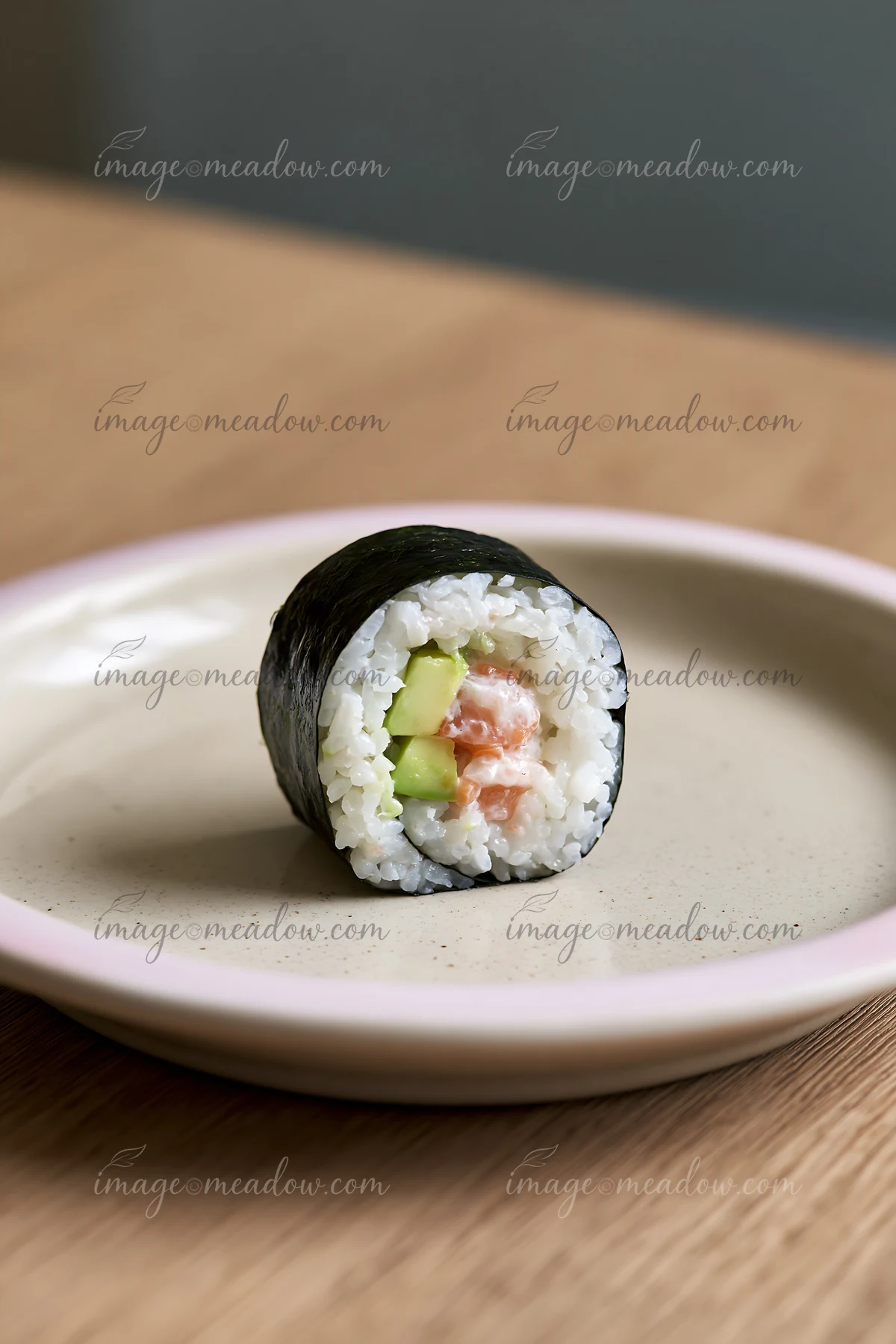A single sushi roll on ceramic plate sits on a wooden table.