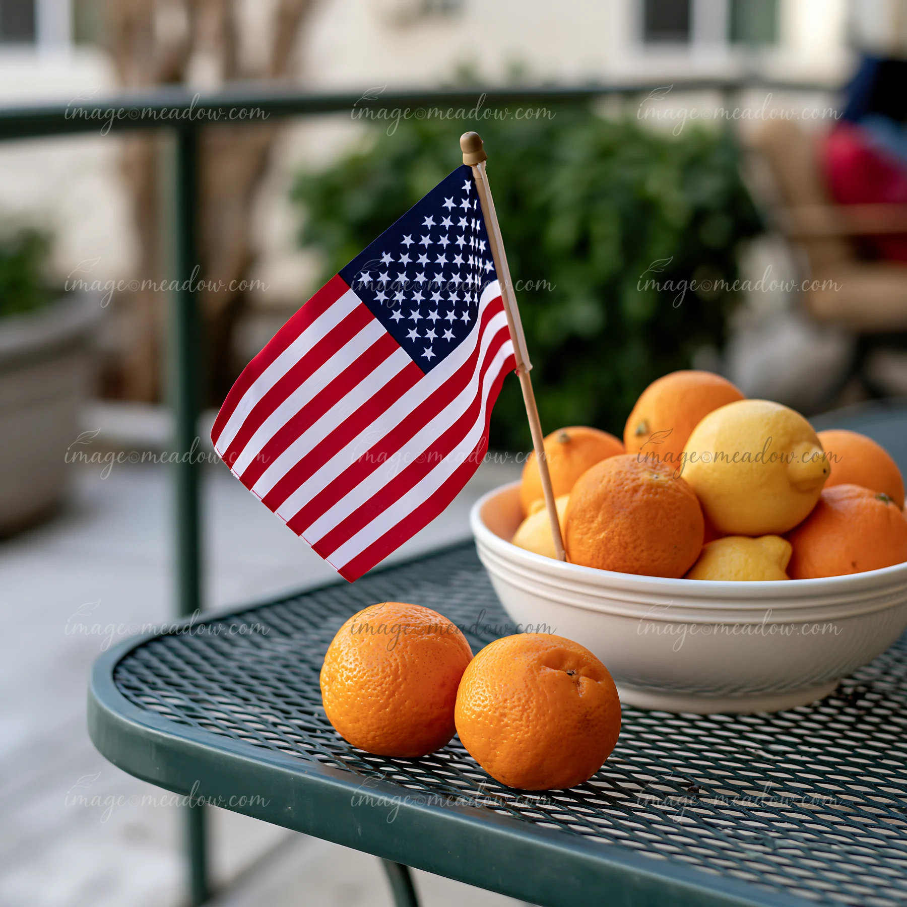 A small American flag stands next to a bowl filled with oranges and lemons on a patio table.