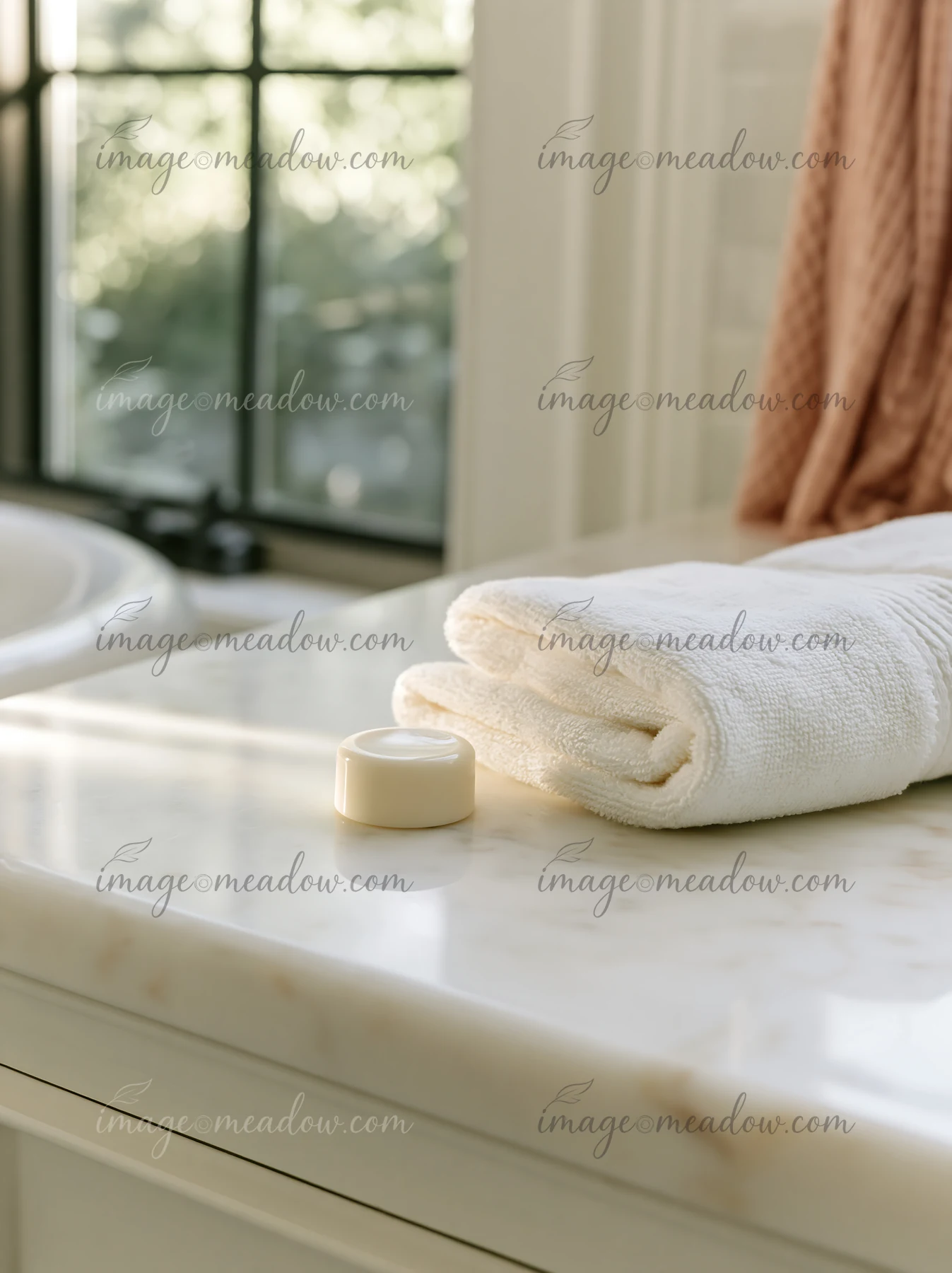 A small cream dose is placed on a marble countertop next to a rolled white towel in a well-lit bathroom.