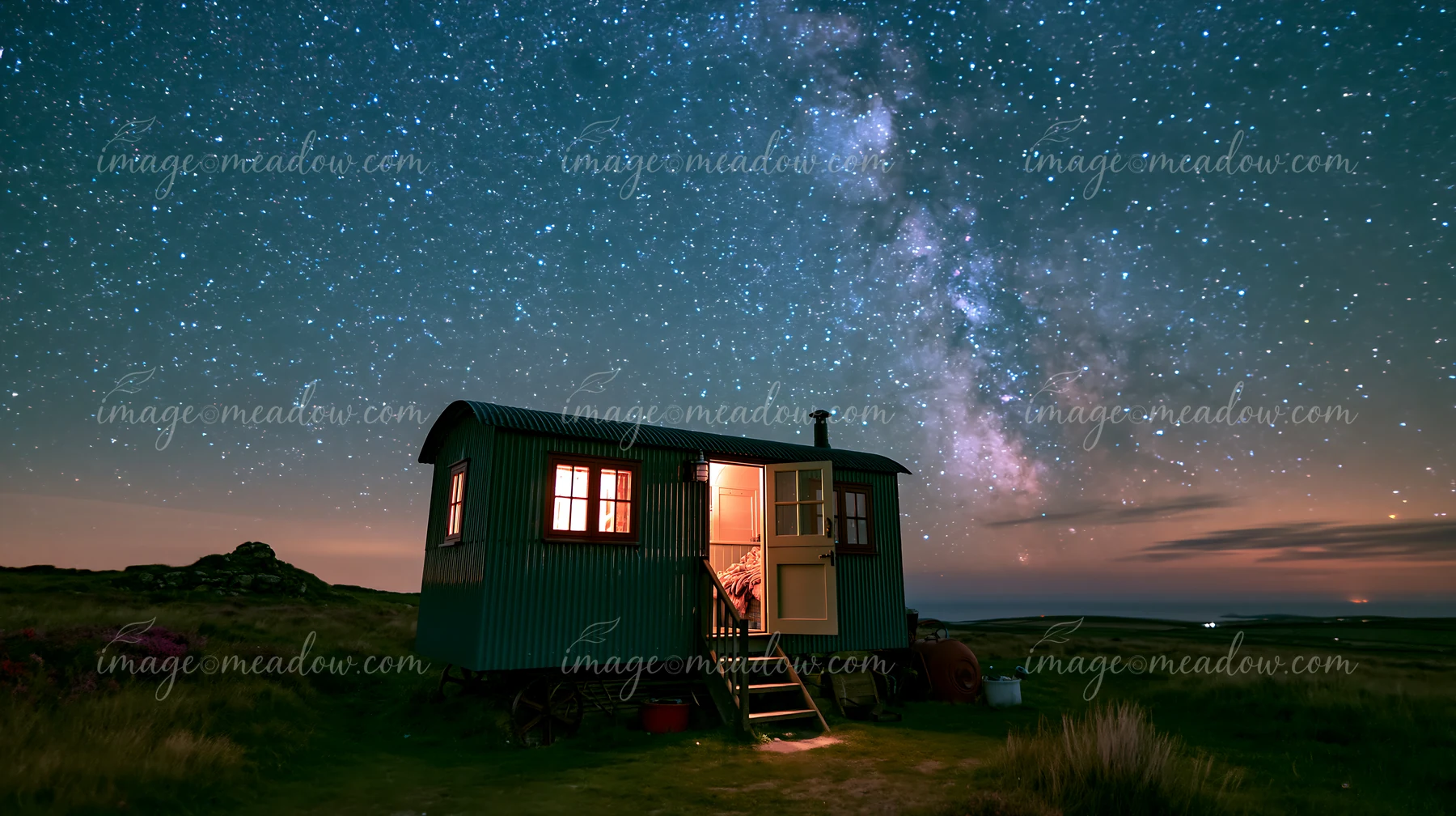 A small home beneath stars in the wilderness sits alone in the open field, illuminated by the glow of windows.