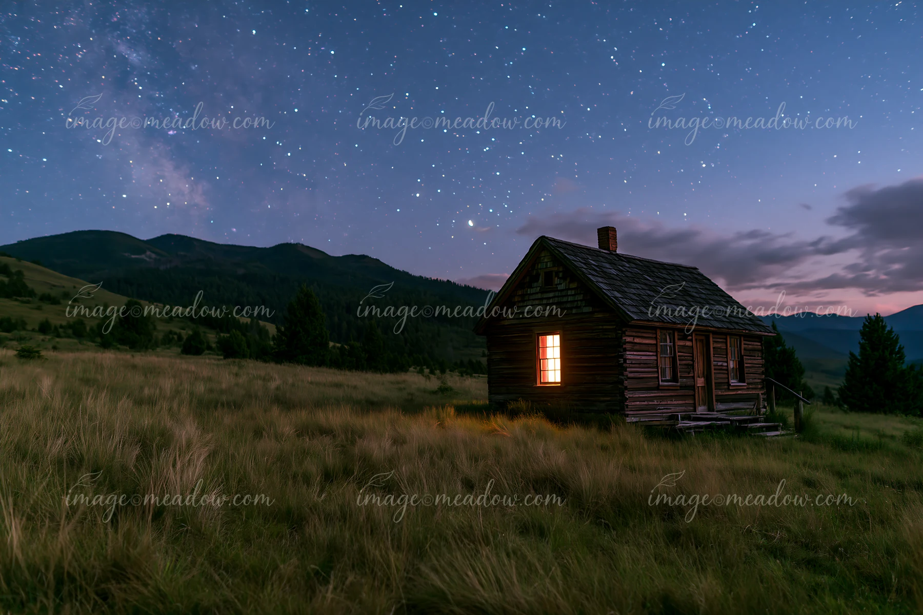A small home beneath stars in the wilderness stands alone against a mountain backdrop.