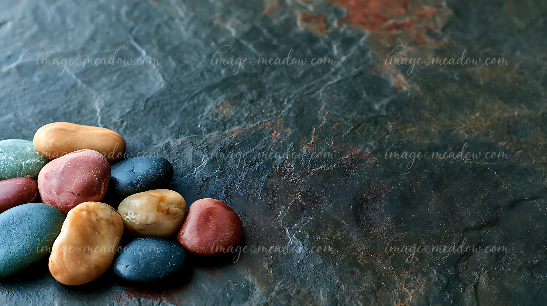 A small pile of smooth, colorful pebbles rests on a textured dark stone surface.