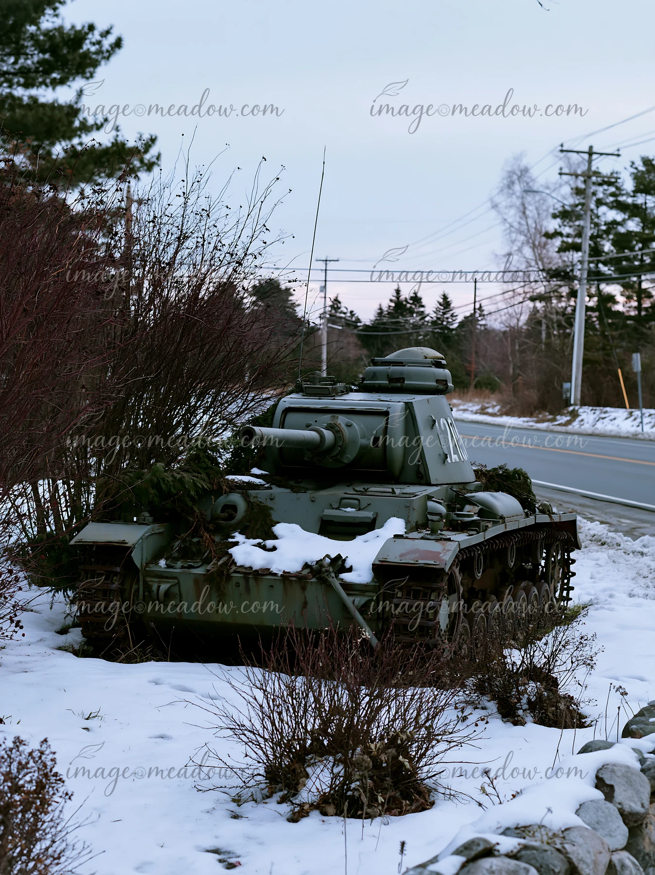 A soldier is positioned under camouflage netting near an old tank in a snowy area.