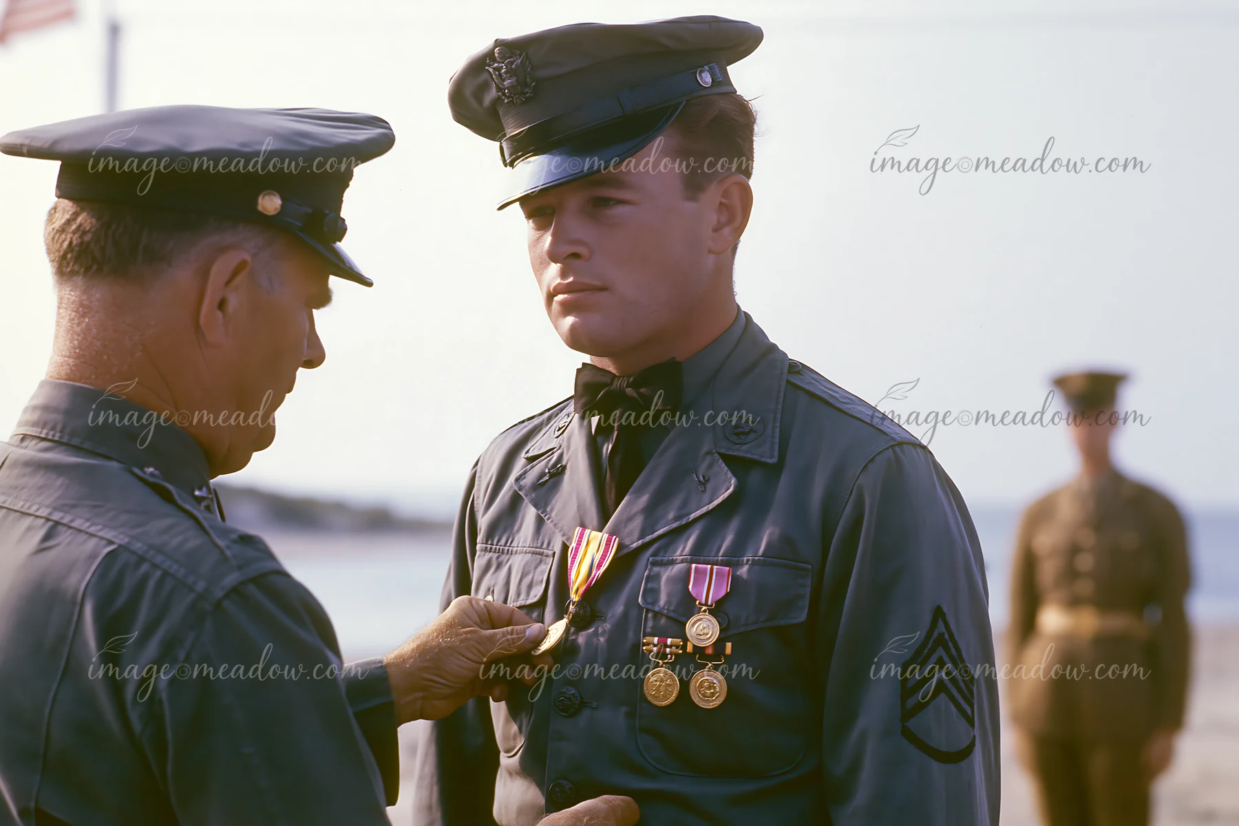 A soldier receiving a medal during an outdoor ceremony stands in uniform while a superior officer pins the medal on his chest.