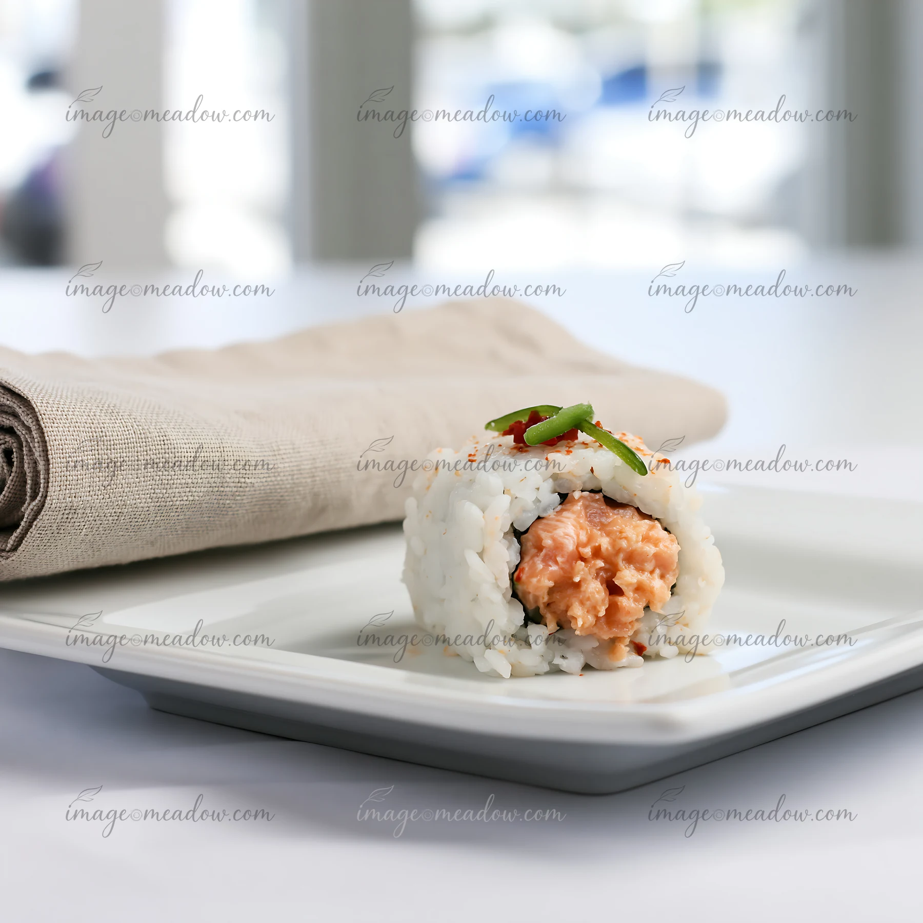 A spicy salmon sushi roll with chili sits on a white plate next to a cloth napkin.