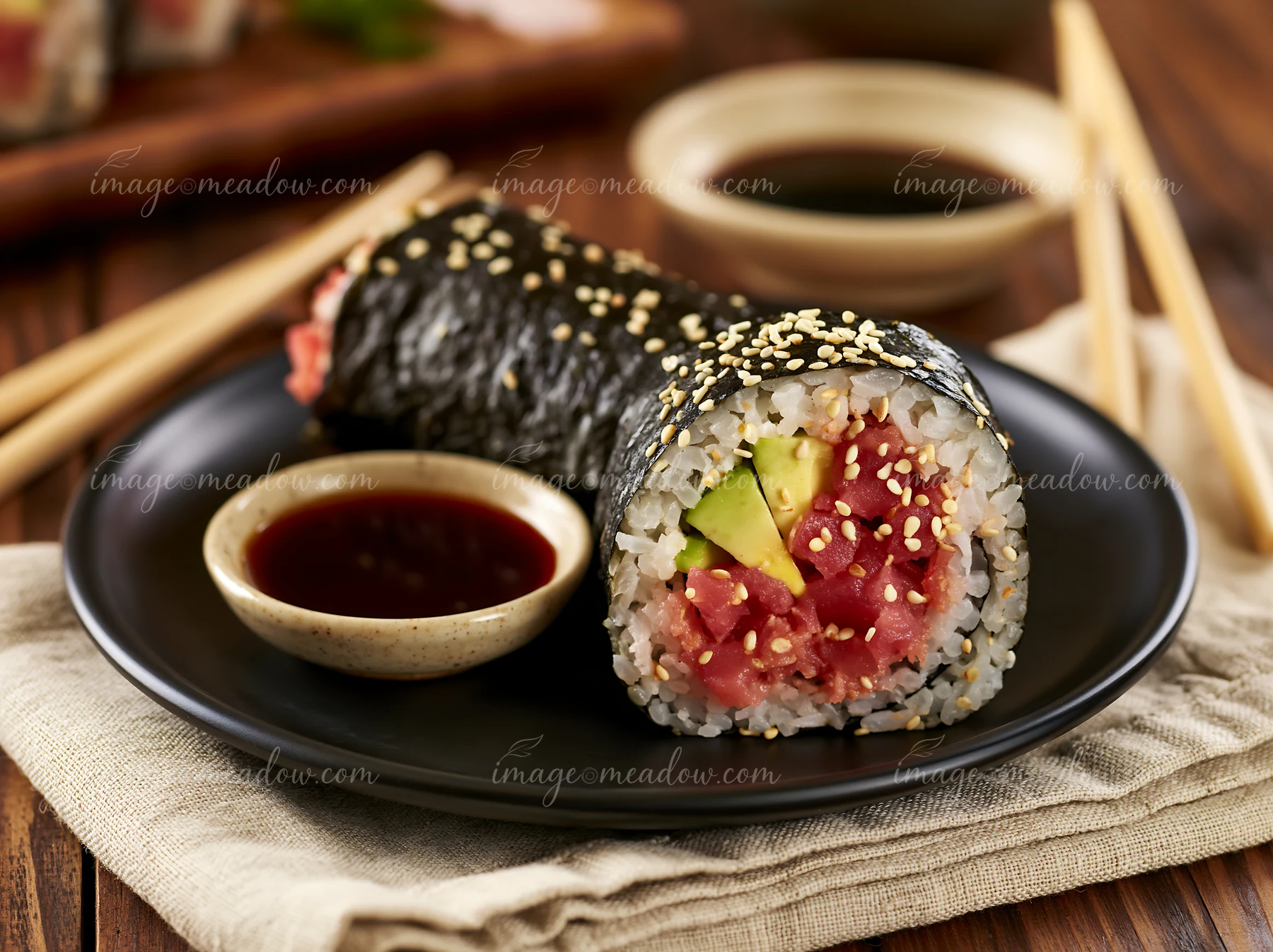 A spicy tuna roll is placed on a black plate next to a small bowl of dipping sauce.