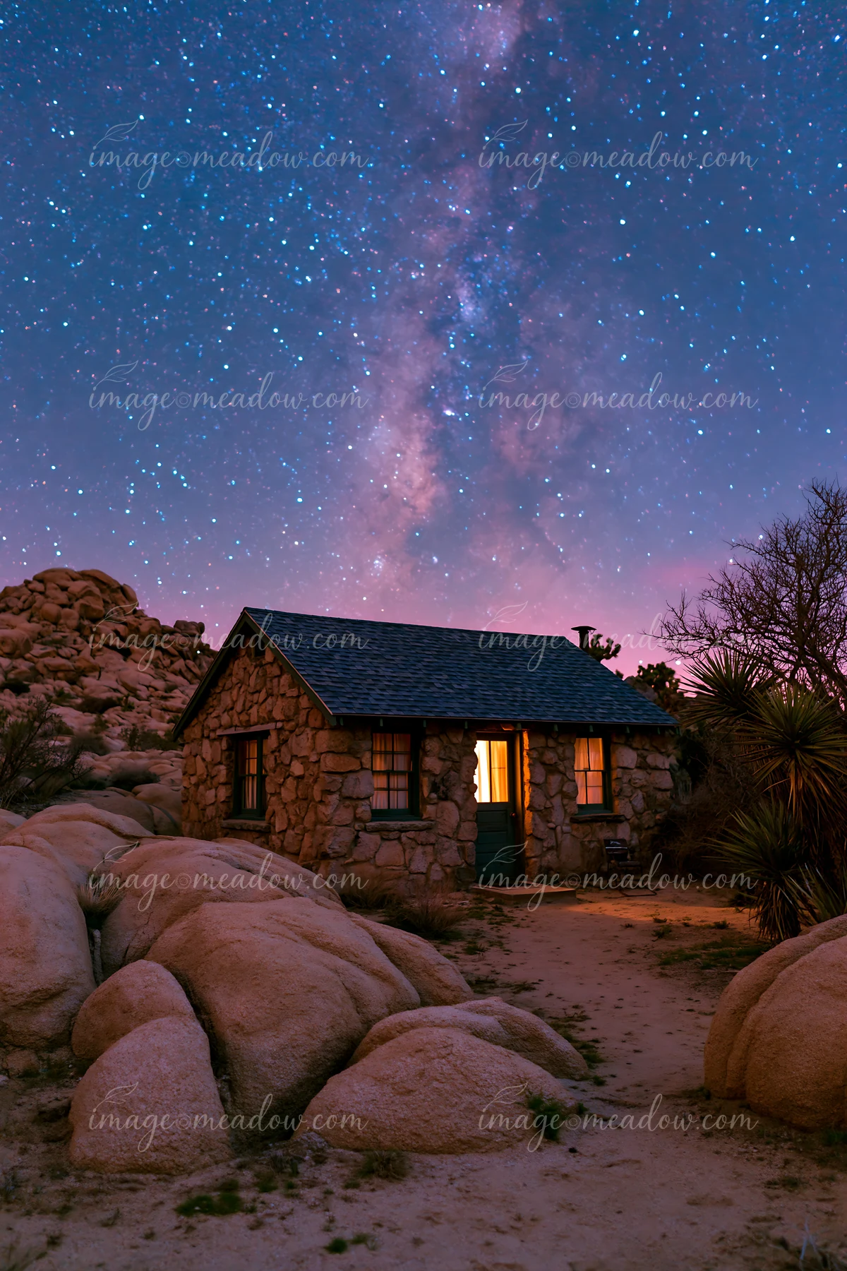 A stone home stands under a starry sky illuminated by the Milky Way.