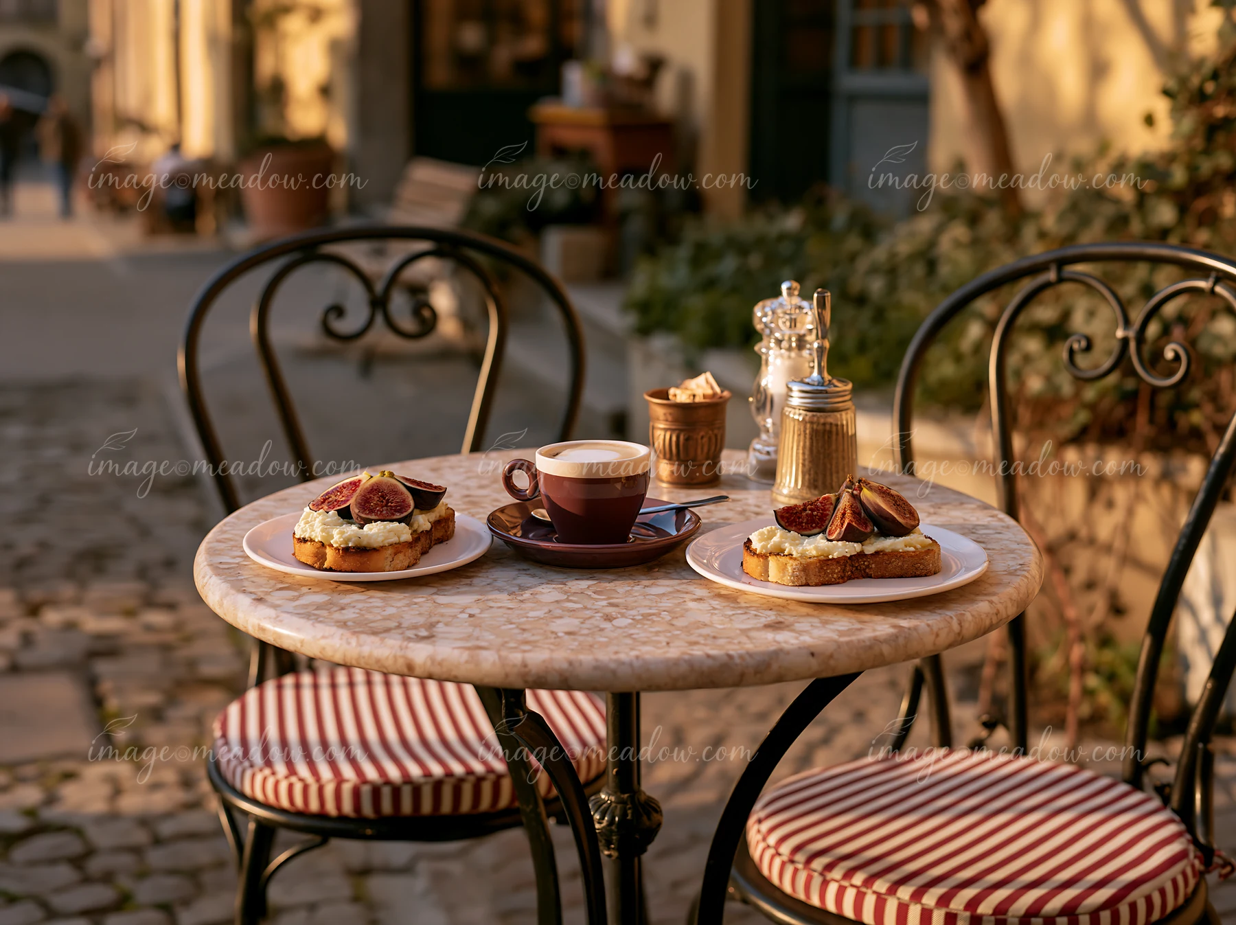 A street cafe table displays two plates of breakfast and a cup of milk coffee.