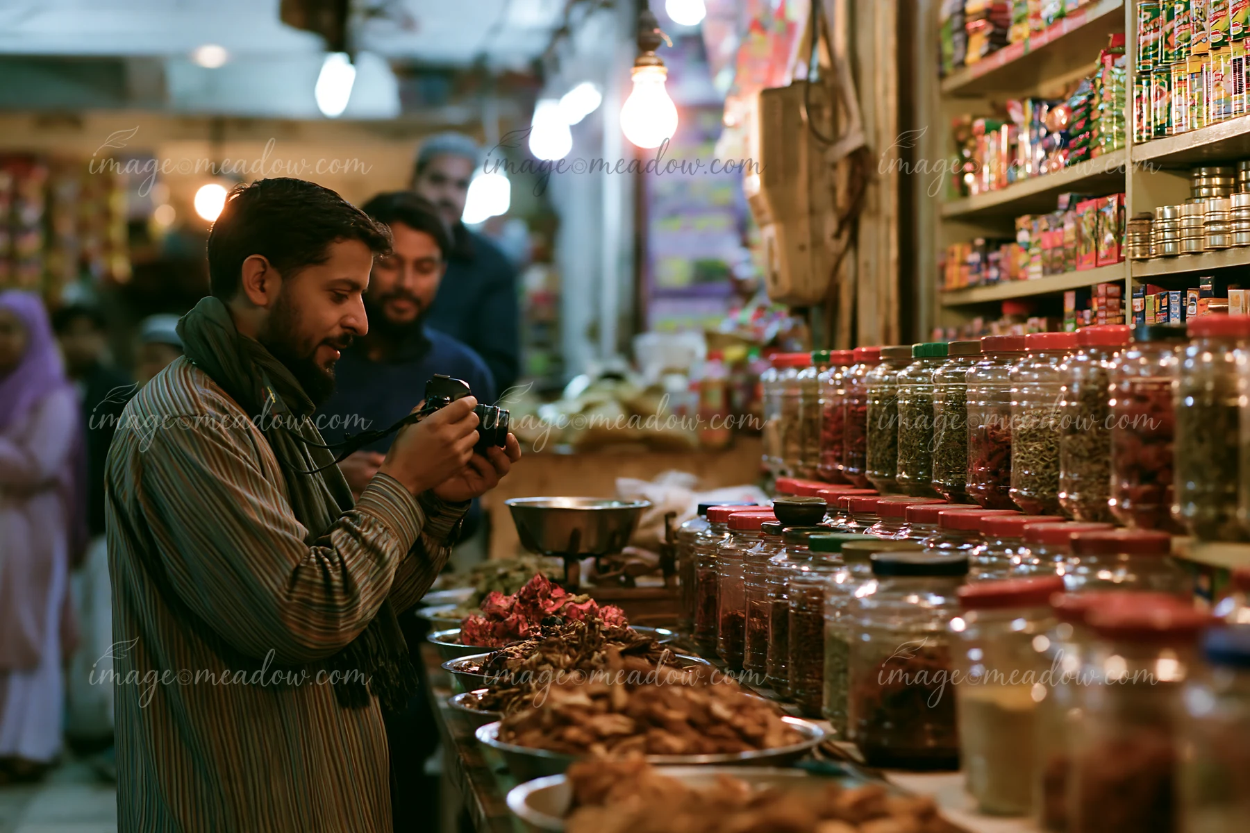A street photographer taking pictures in an urban market stands by a spice stall filled with jars.