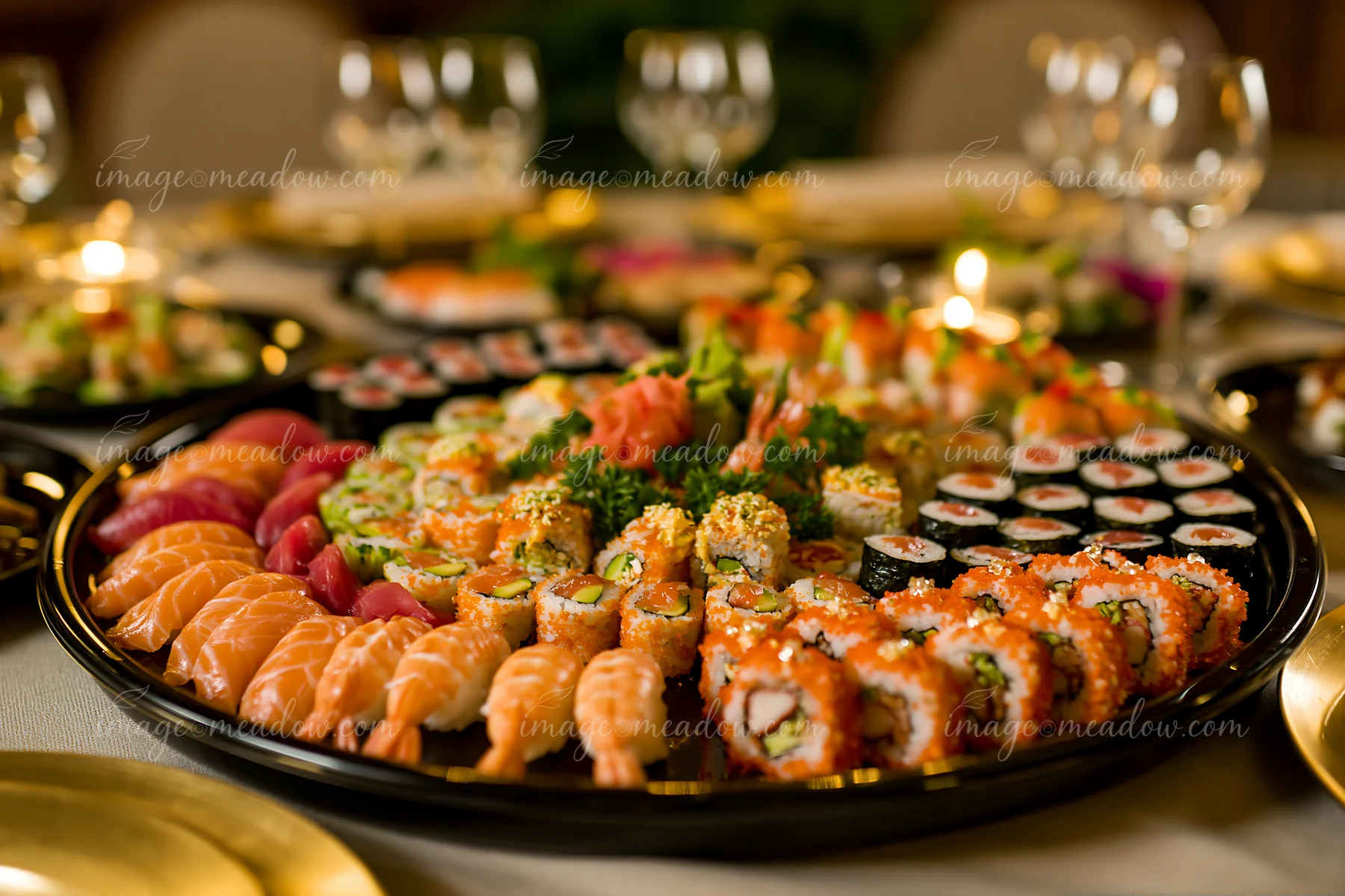 A sushi catering platter displays a variety of sushi types, including rolls, sashimi, and nigiri, set on a table ready for an event with glassware and decorativ