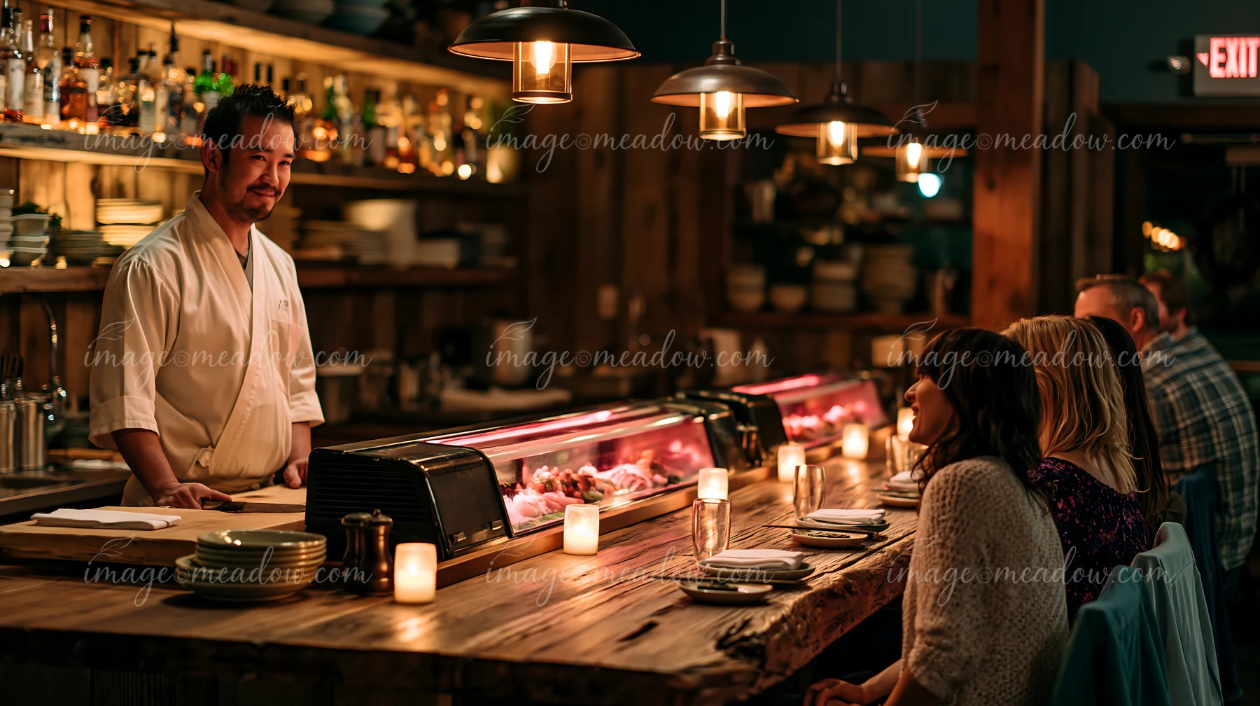 A sushi chef greets diners in a warm restaurant filled with wooden decor.