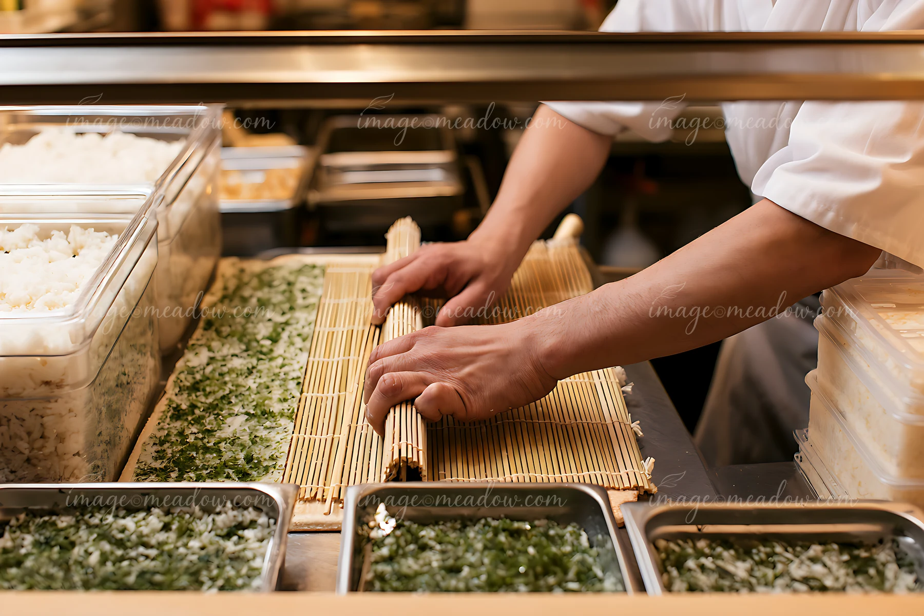 A sushi chef rolls maki using a bamboo mat while preparing sushi in a restaurant.