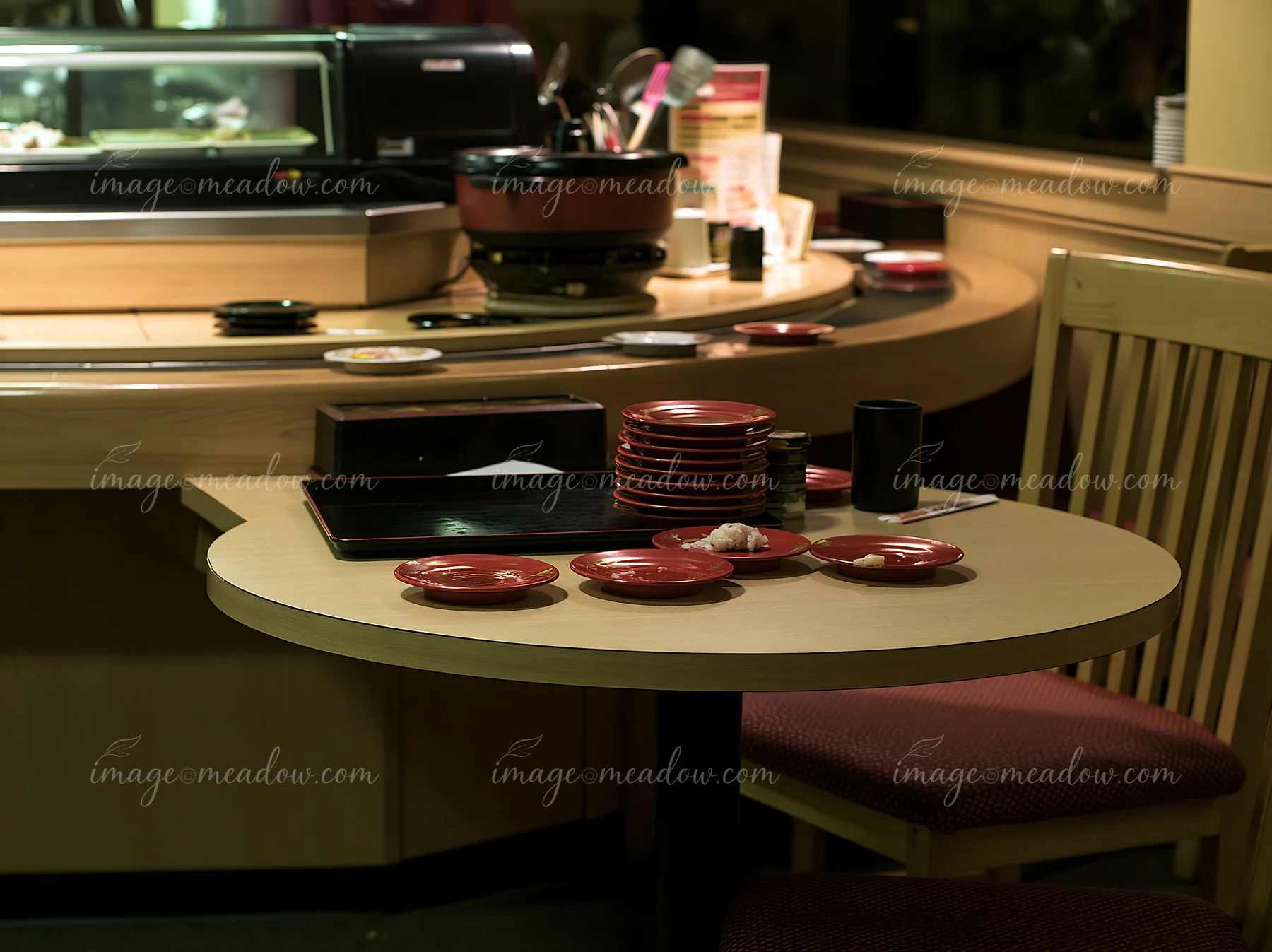 A table in a sushi conveyor belt restaurant shows several empty red plates stacked up.